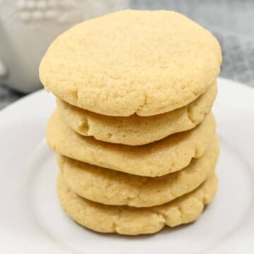 A stack of five round, golden-brown sugar cookies on a white plate.