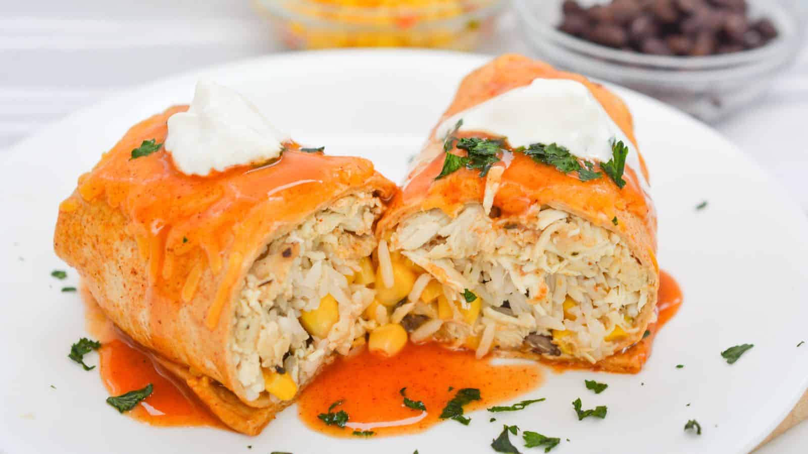 Two chicken enchiladas topped with red sauce and sour cream, garnished with cilantro, served with a side of corn and black beans.