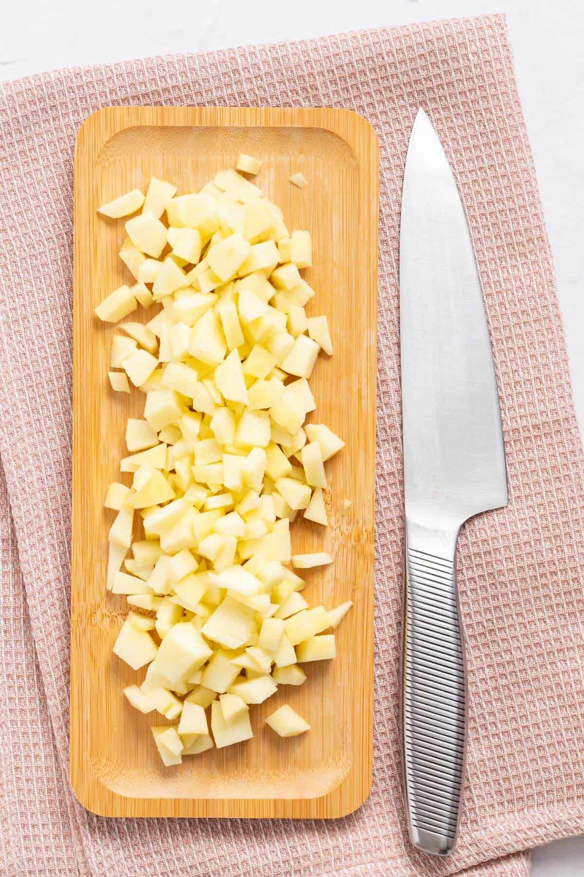 Chopped apples on a wooden cutting board next to a kitchen knife, placed on a pink textured cloth.