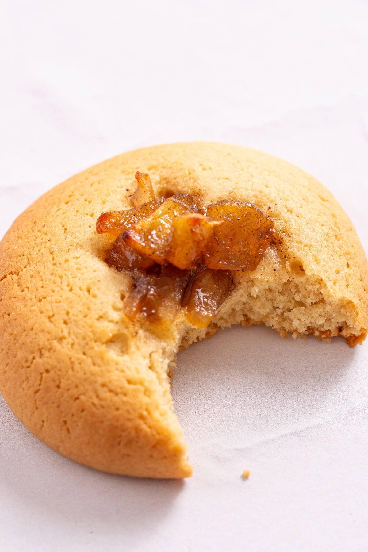 A single round apple pie cookie with a bite taken out, revealing a gooey apple filling.