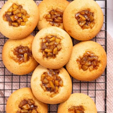 Freshly baked cake cookies topped with caramelized apple chunks, arranged on a cooling rack.