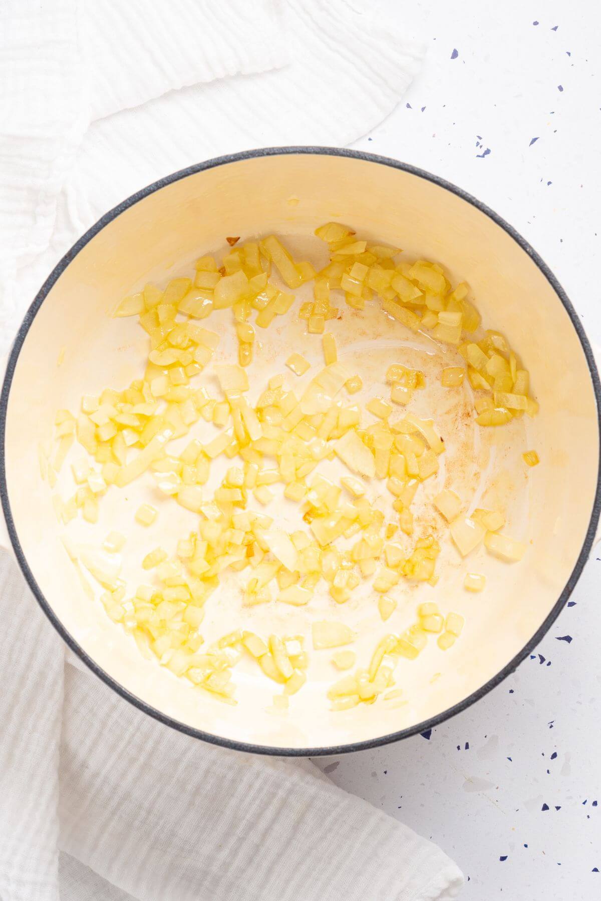 A pot of sautéed chopped onions on a white cloth, with black specks scattered around.