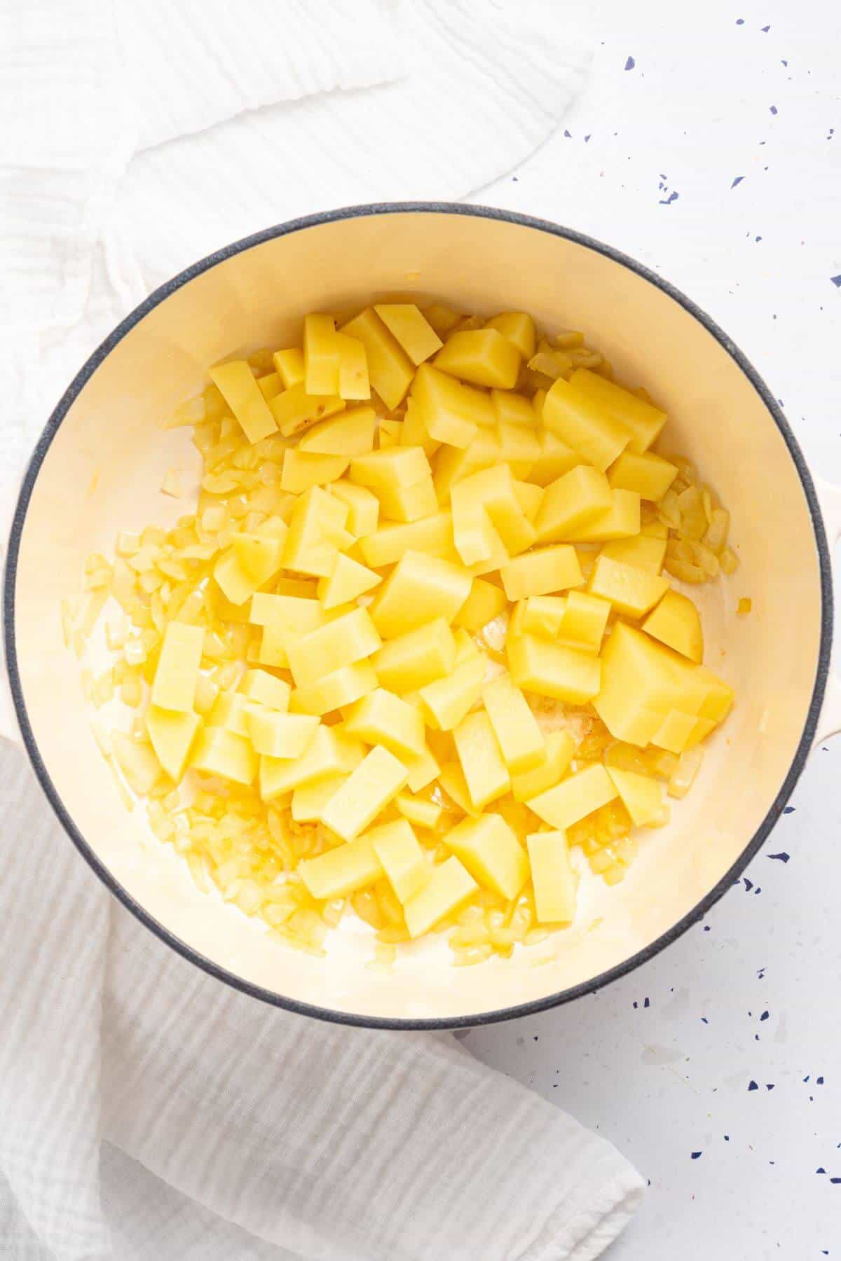 Pot of diced potatoes and chopped onion on a white surface.