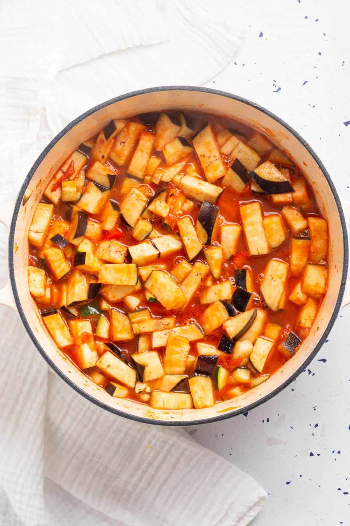 A pot of diced eggplant in a rich, red tomato sauce on a white surface.