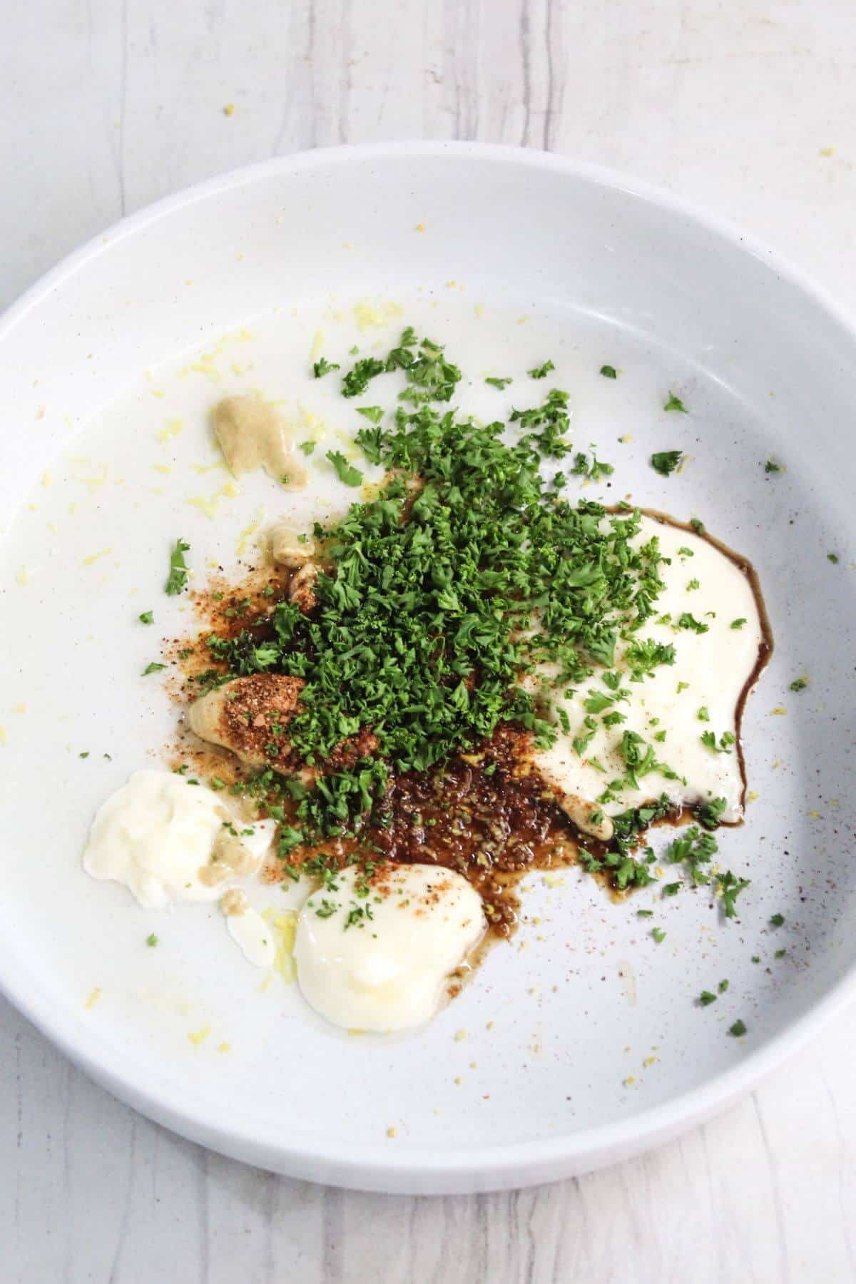 A white plate with dollops of mayo, egg, and mustard over grated lemon zest topped with seasoning and parsley.