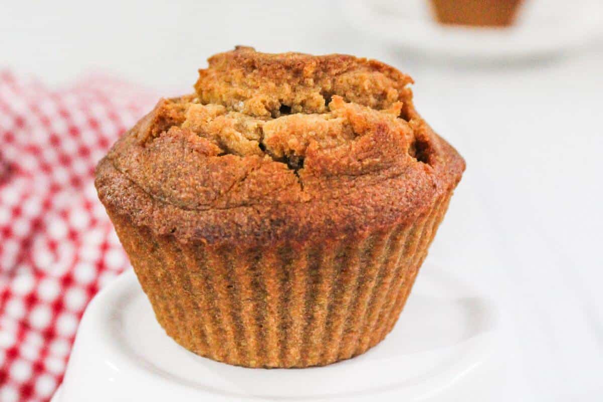 A whole muffin is displayed on a white surface with a red and white checkered cloth in the background.