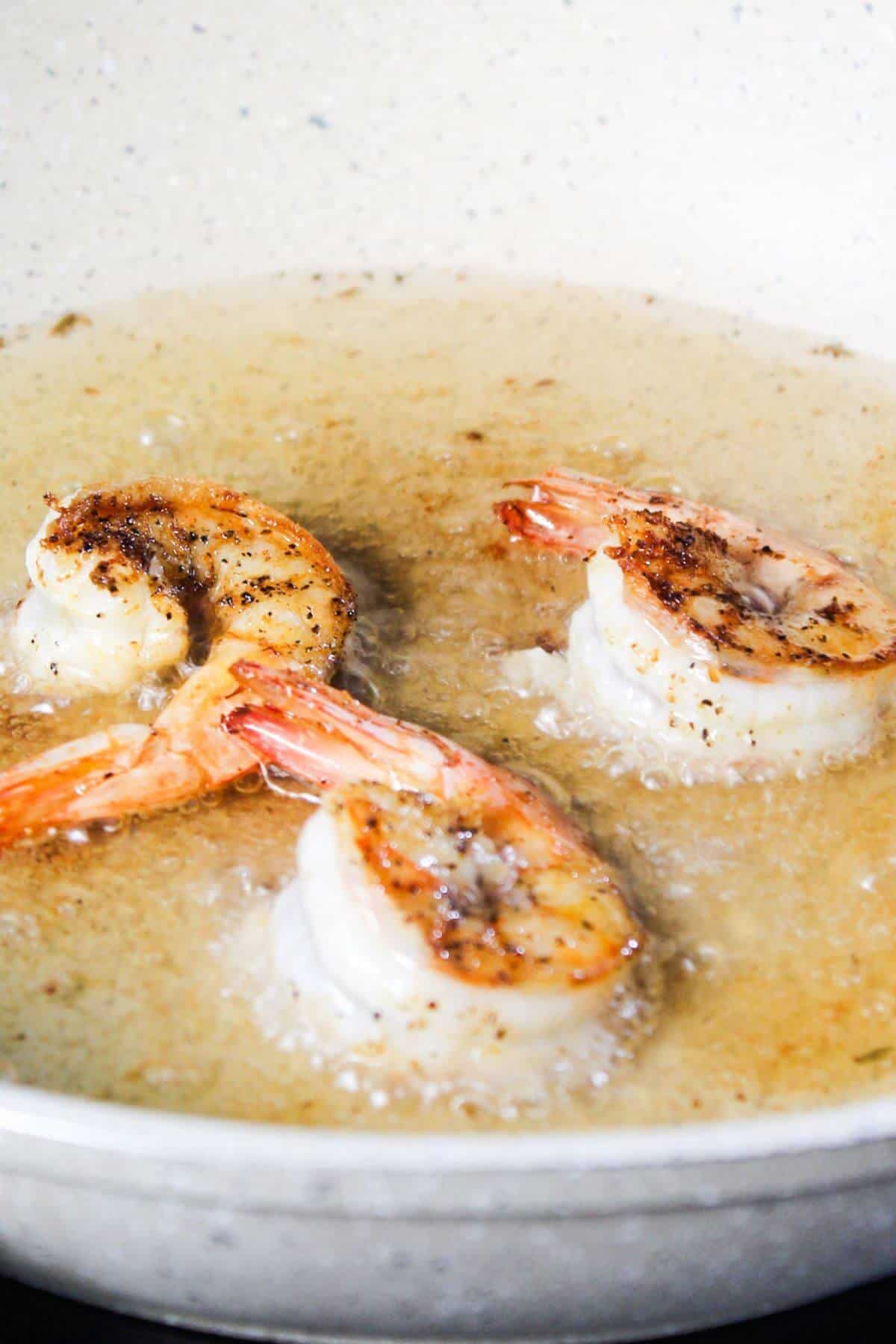 Three shrimp being cooked in a frying pan with bubbling oil.