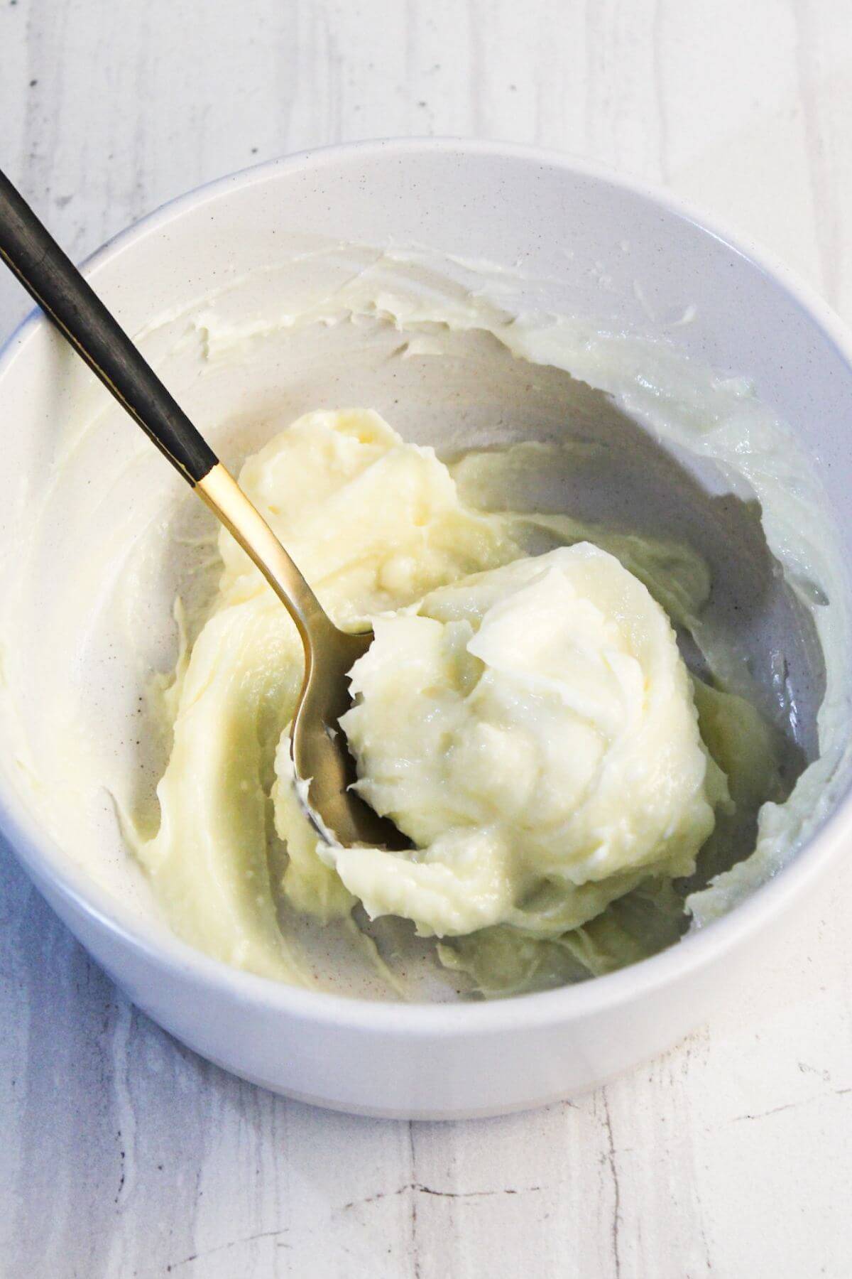 A bowl containing a creamy mixture being stirred with a spoon, reminiscent of the filling in a cream cheese danish. The consistency appears smooth and thick.