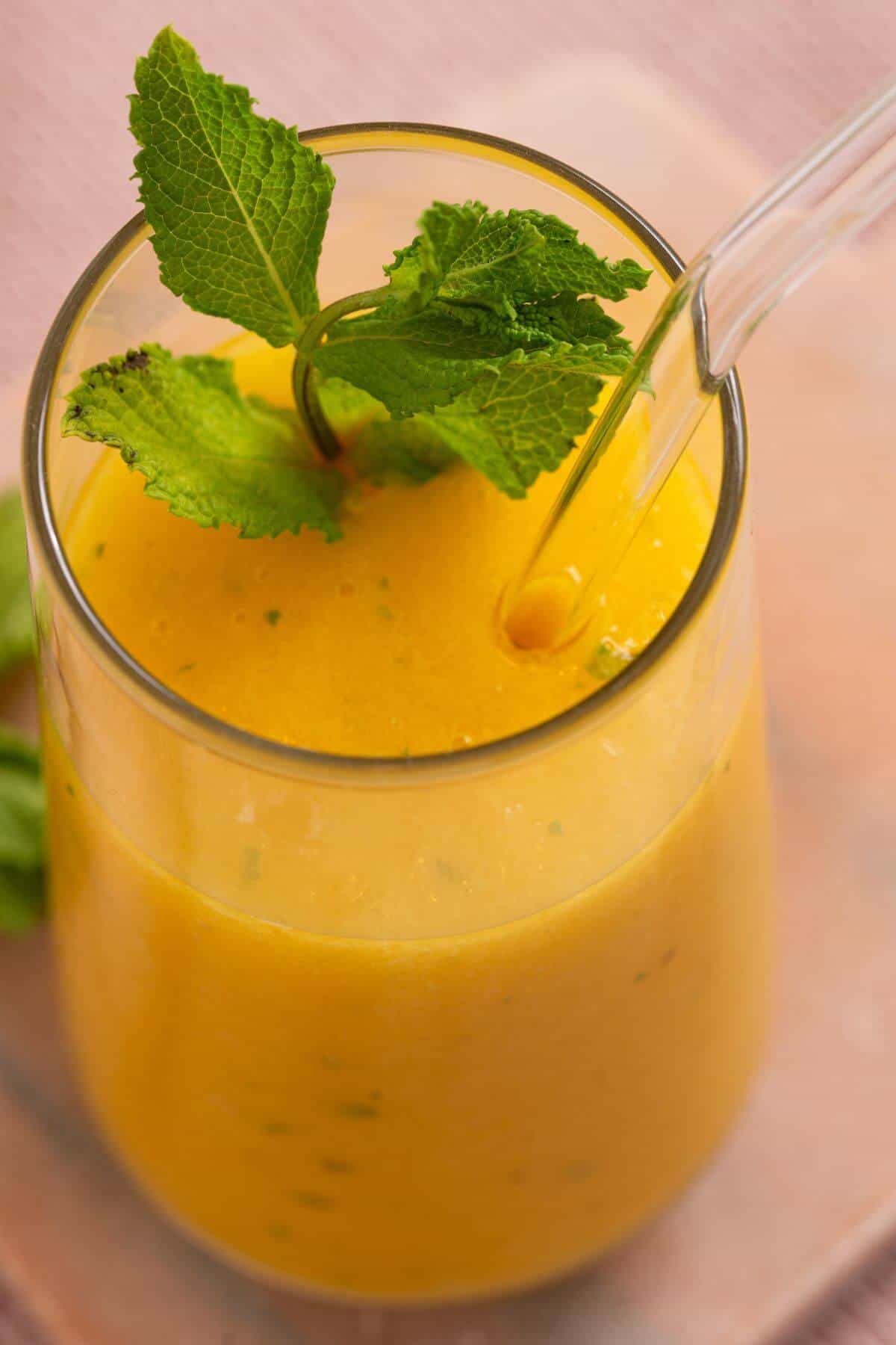 A glass of bright orange smoothie garnished with fresh mint leaves and a clear straw.