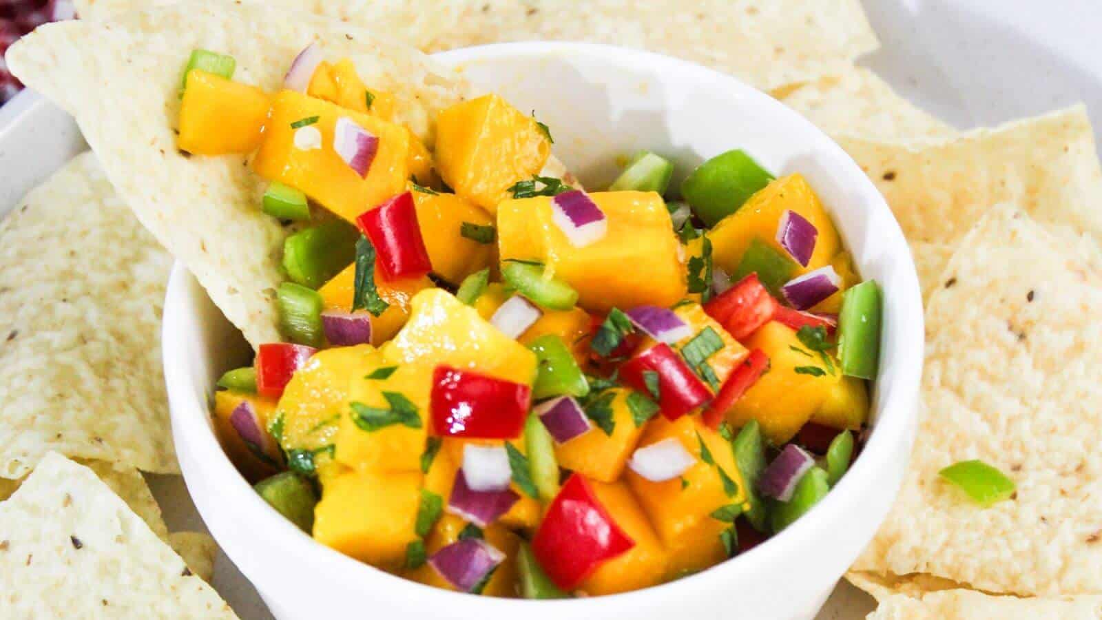 A bowl of fresh mango salsa with diced mango, red onion, red bell pepper, and green bell pepper, served with tortilla chips.