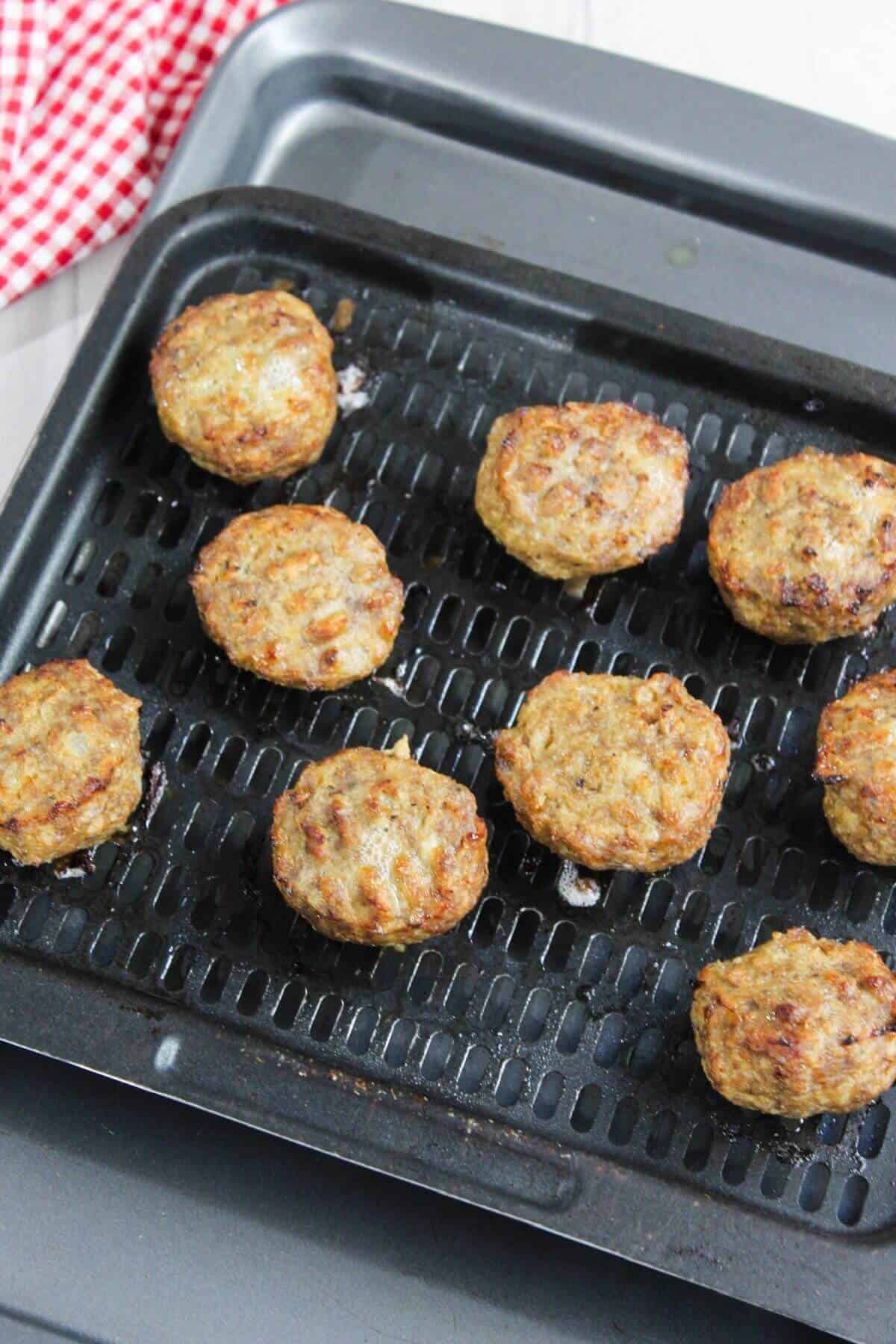 Nine meatballs on an air fryer tray, with a red and white checkered cloth partially visible in the background.