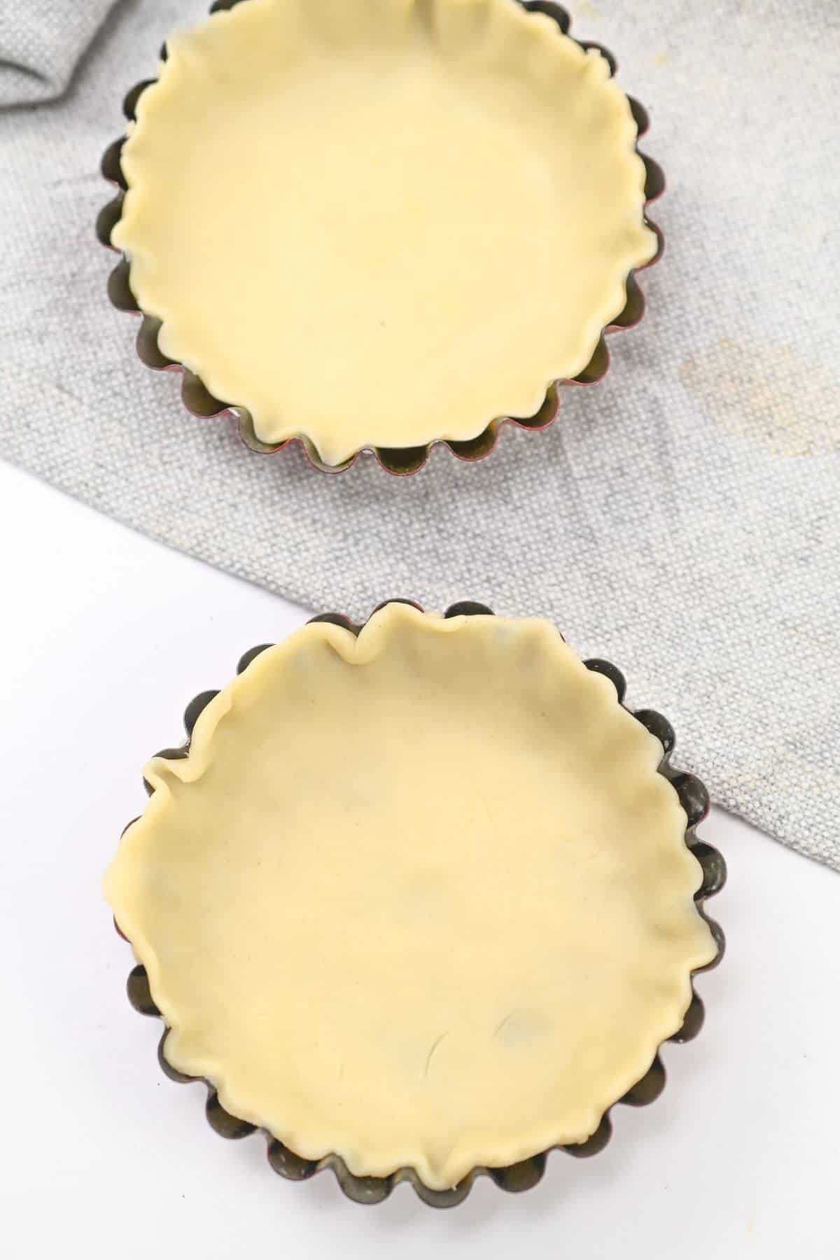Two mini pie crusts on a table next to each other.