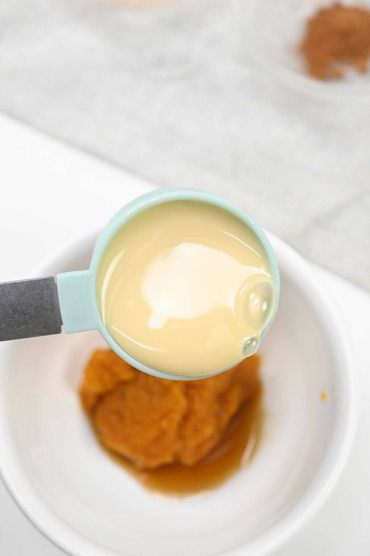 A spoon with condensed milk pouring into a bowl of pumpkin purée.