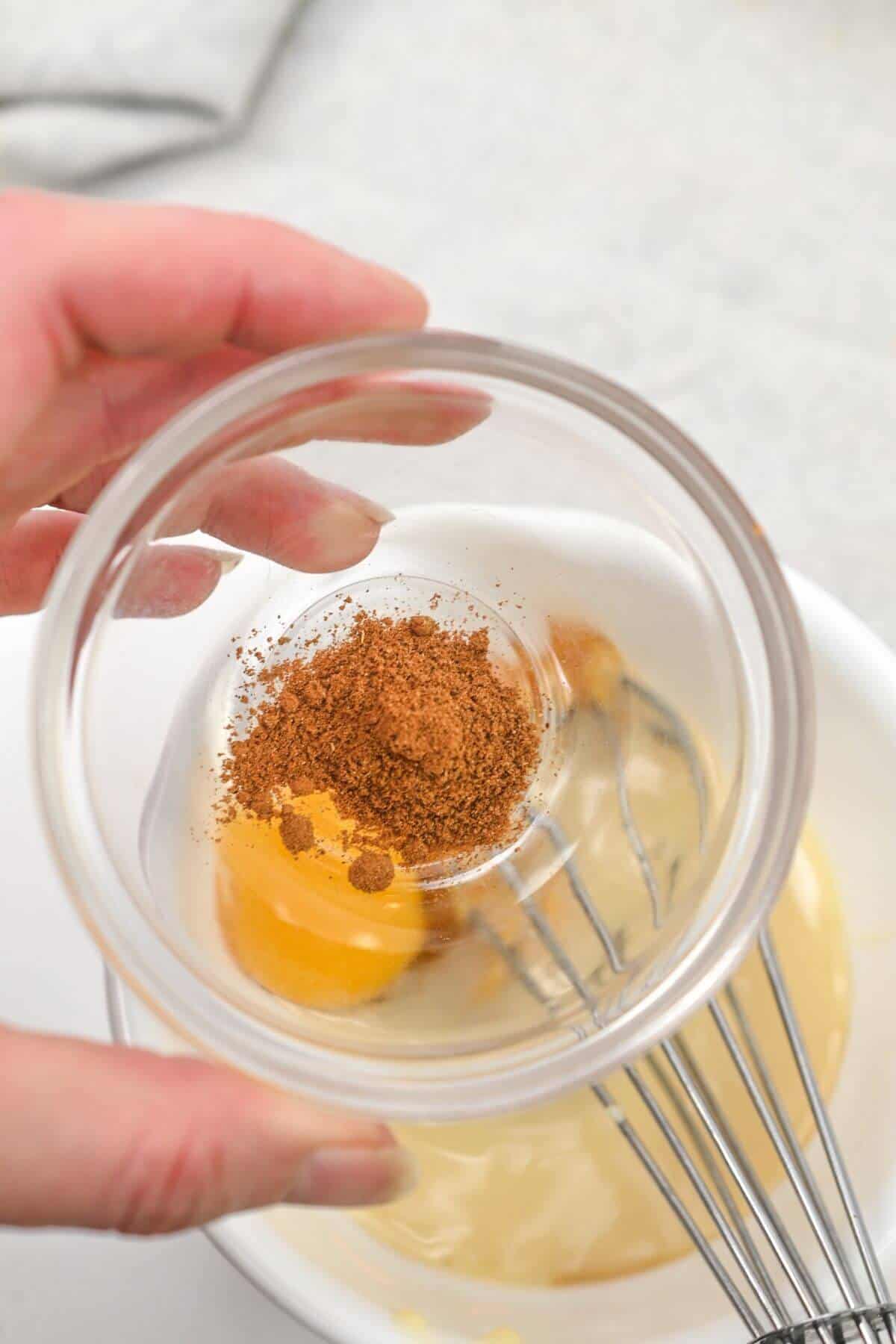 A person mixing ingredients in a bowl with a whisk.