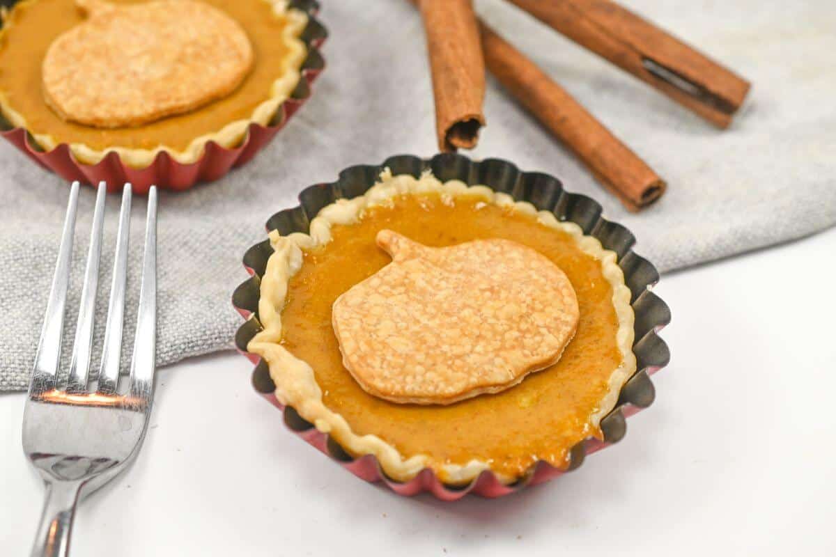 Two pumpkin pies with cinnamon sticks and a fork.