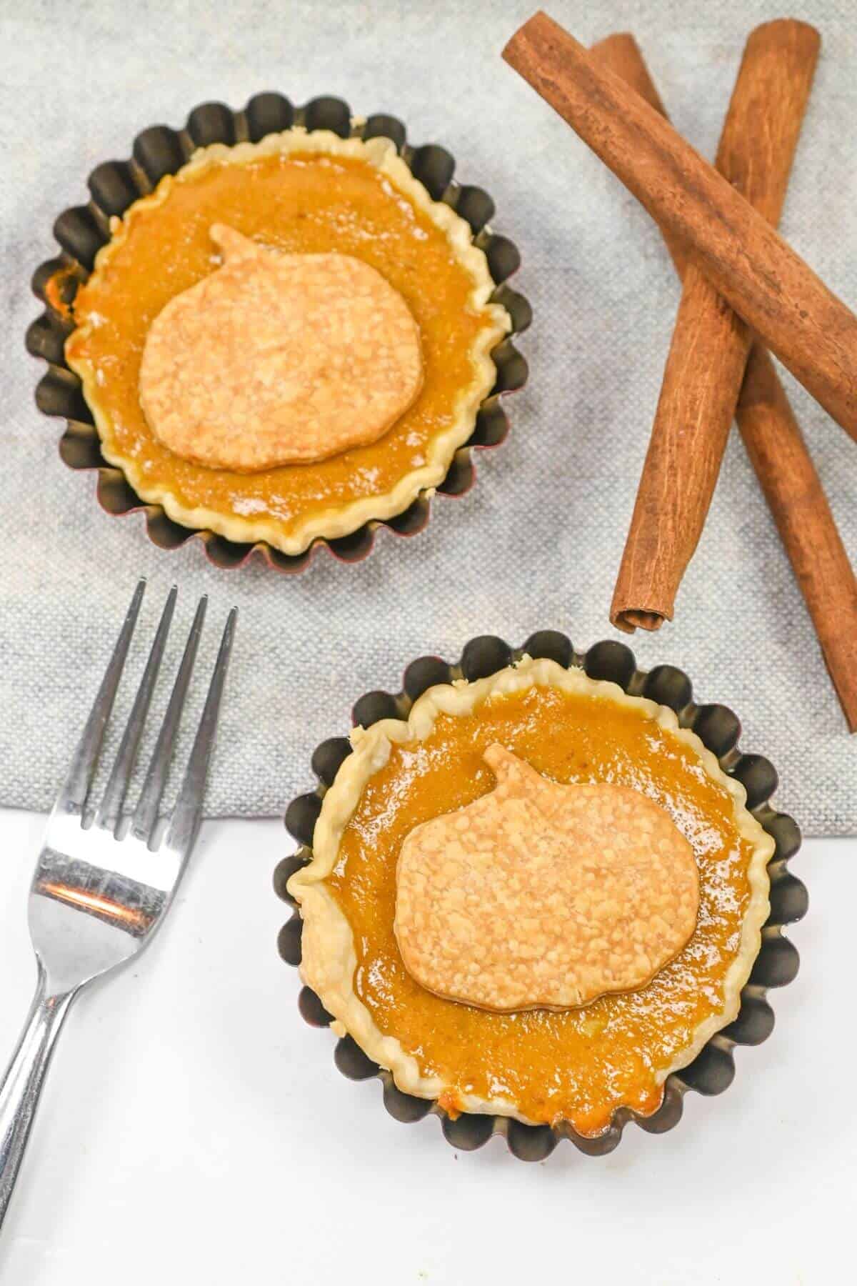 Pumpkin tarts in mini tart tins with cinnamon sticks and a fork.