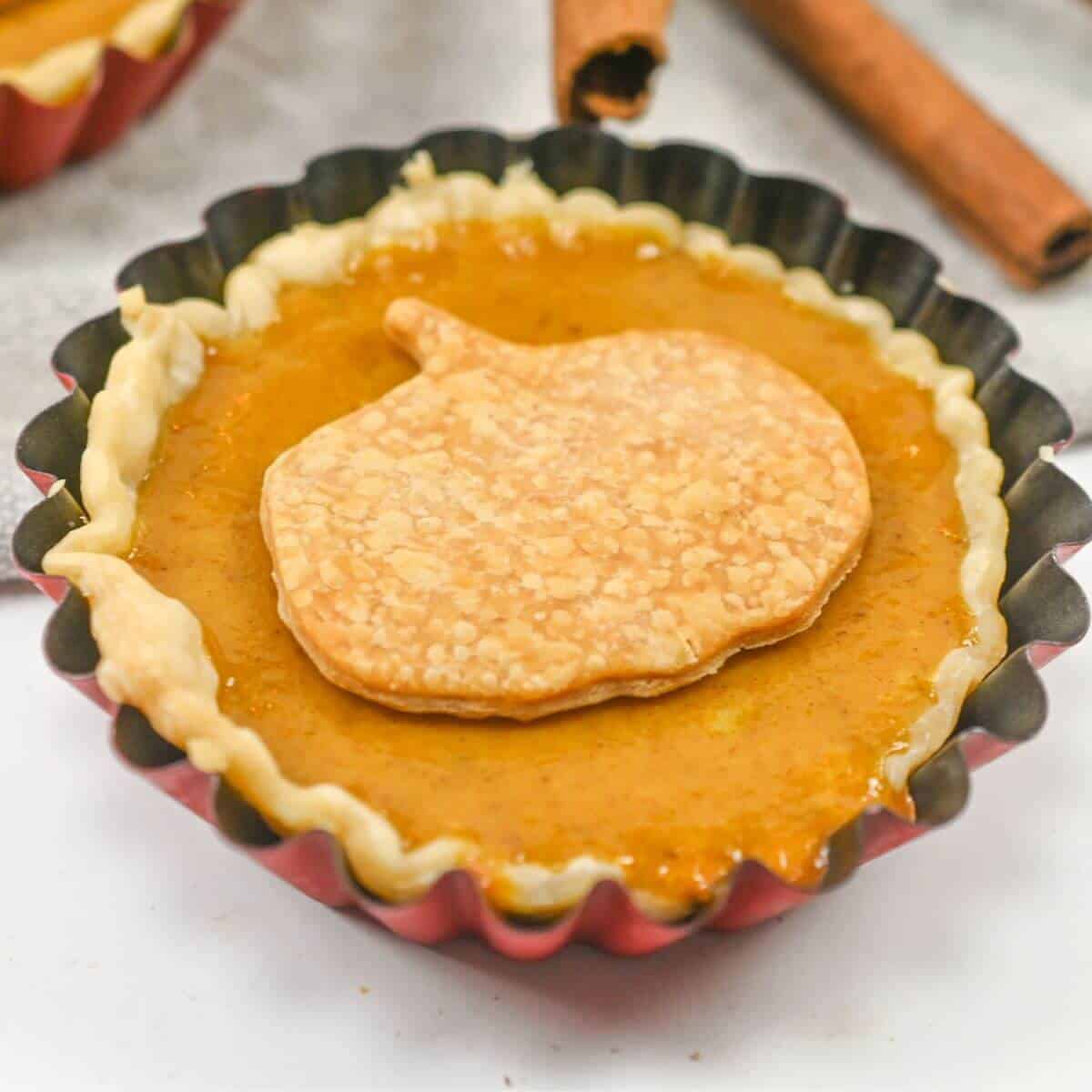 Mini pumpkin pie in a tart tin with cinnamon sticks.