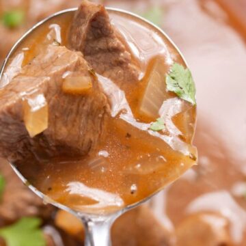 Close-up of a spoonful of beef stew with chunks of meat, onions, and parsley in a rich brown broth.
