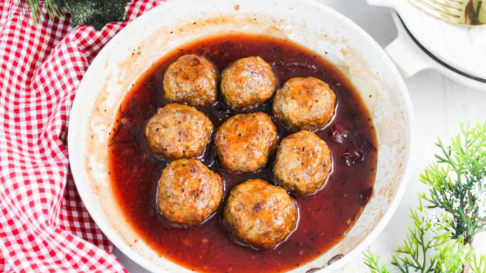 A bowl with eight browned ground turkey meatballs in a sauce, placed on a red and white checkered cloth.