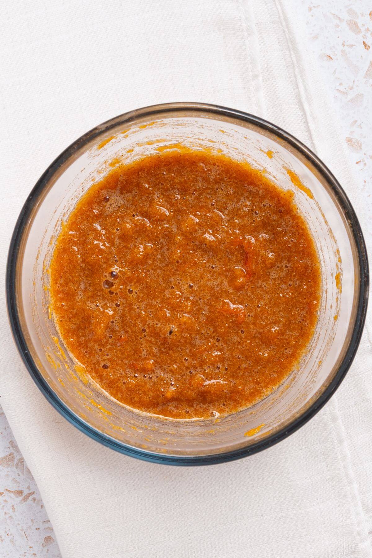 A glass bowl containing a thick pumpkin mixture sits on a white cloth.