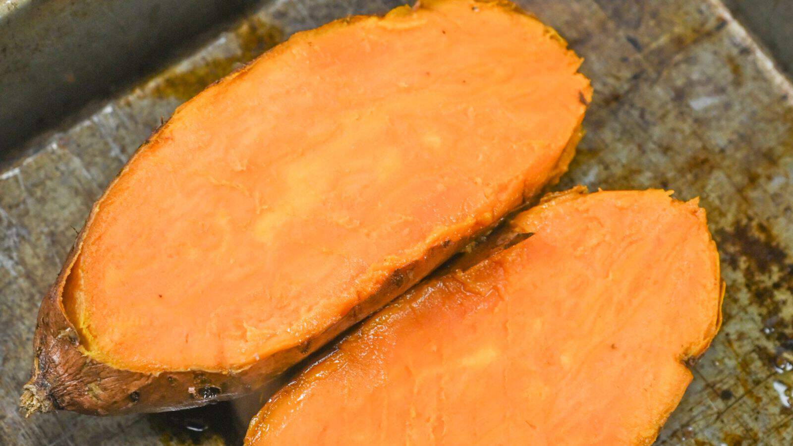 Close-up of a halved roasted sweet potato on a metal surface, showcasing its bright orange flesh.