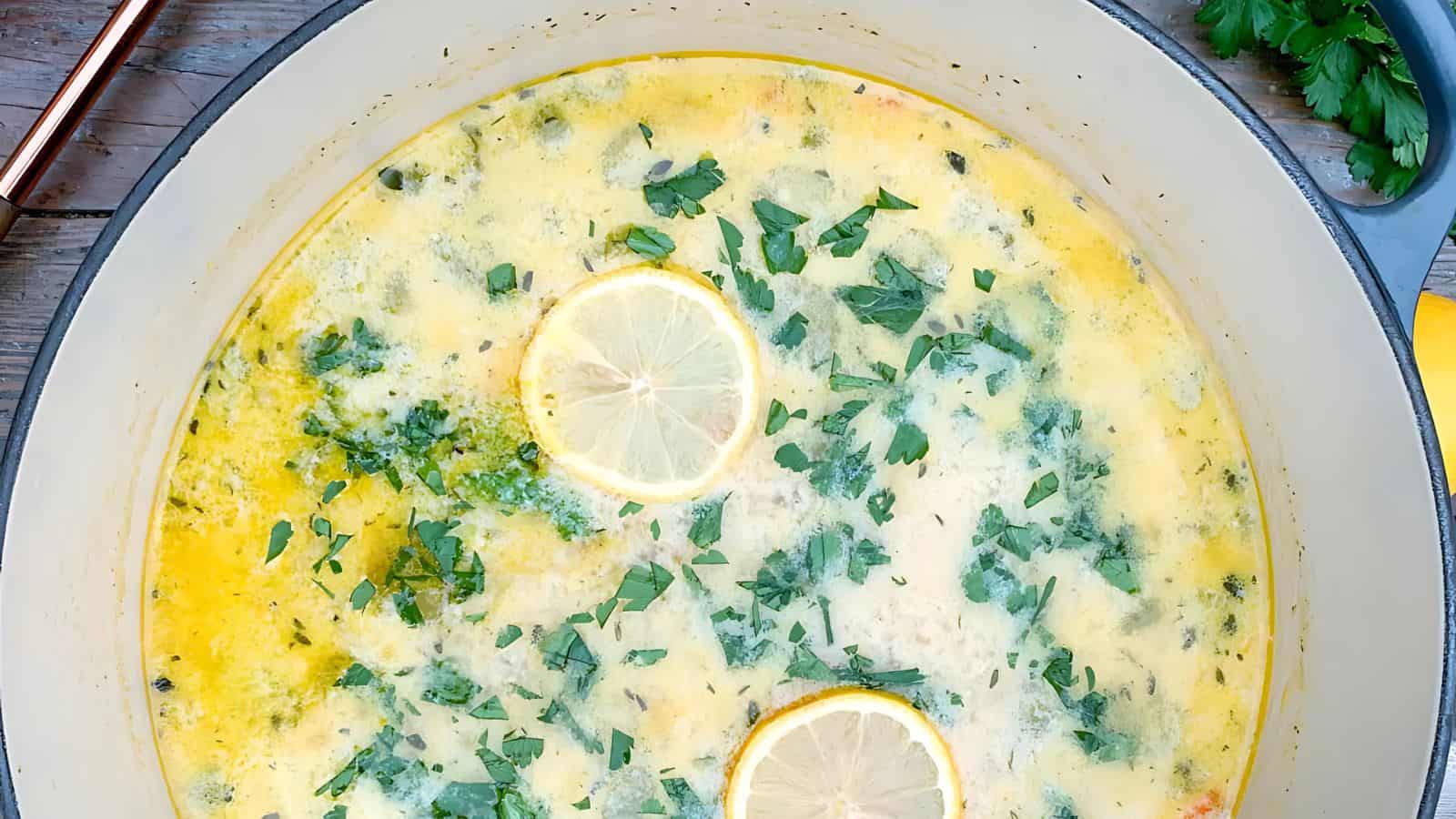 A pot of lemon herb soup topped with parsley and lemon slices.