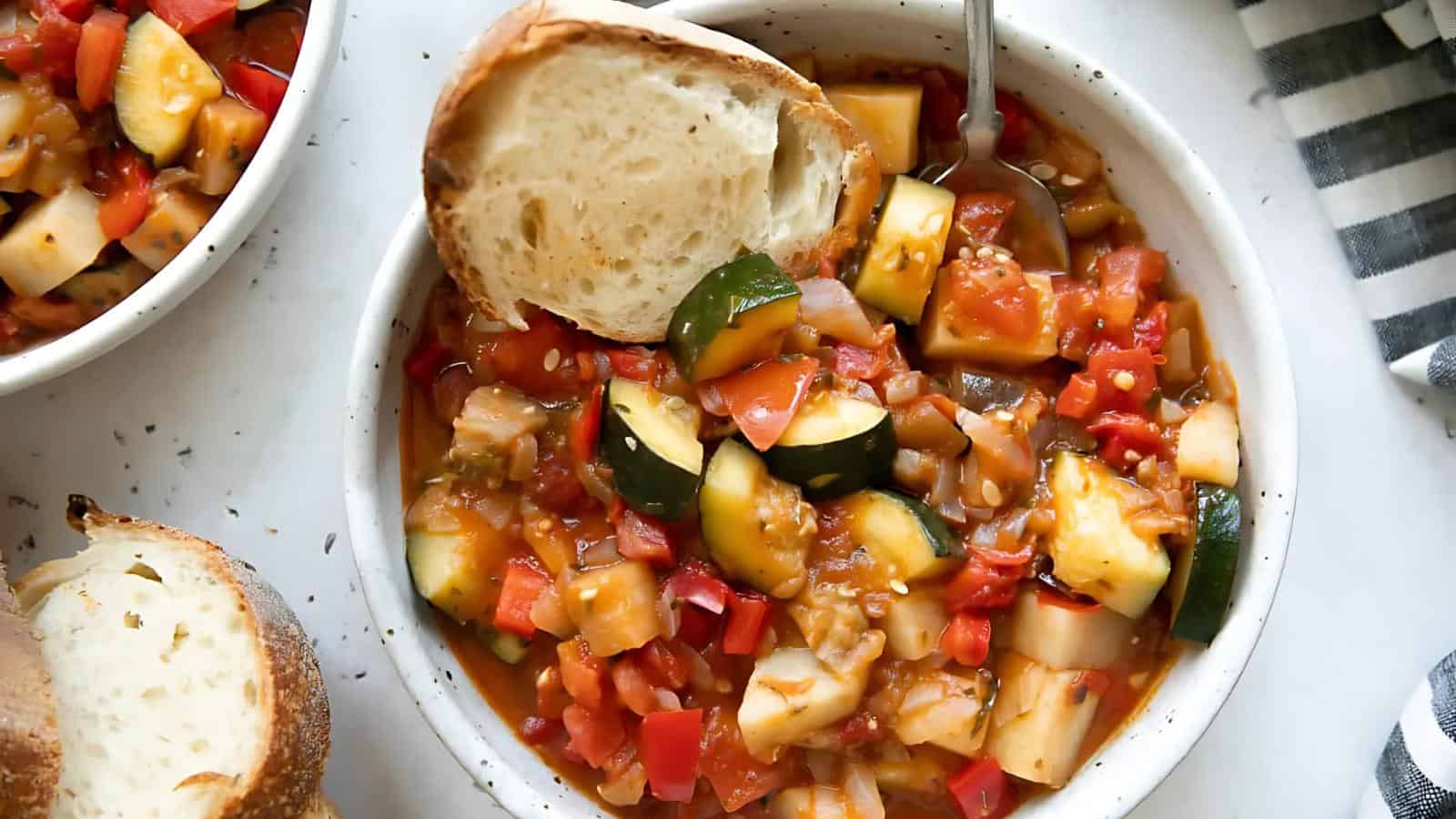 Bowl of vegetable stew with zucchini, tomatoes, and bell peppers, topped with a slice of bread.