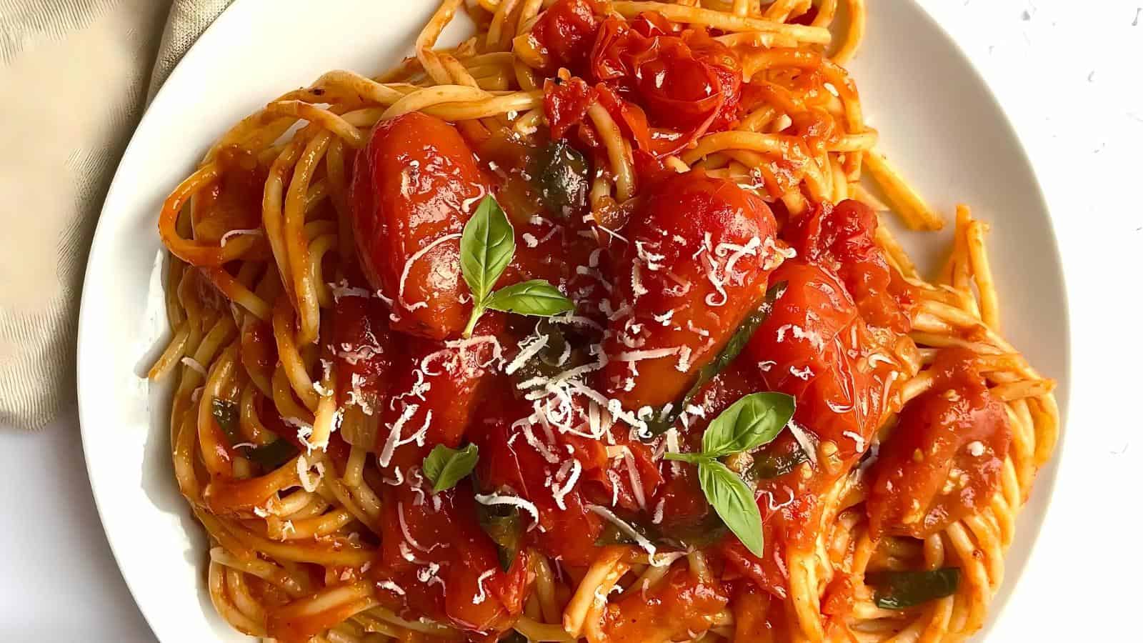 A plate of spaghetti with tomato sauce, topped with grated cheese and basil leaves.