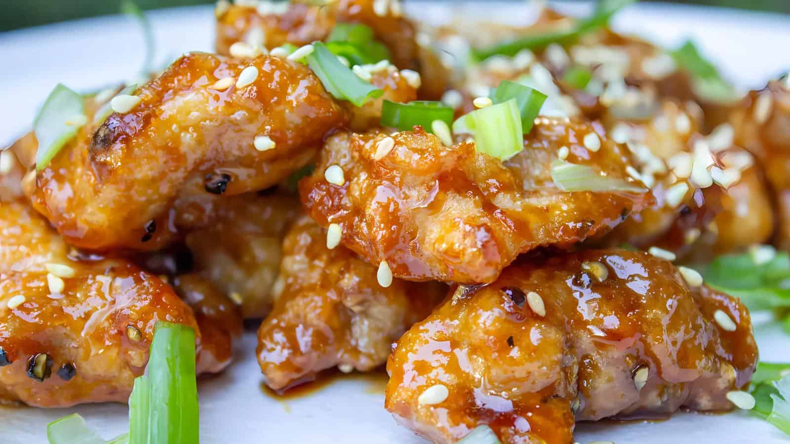 A plate of glazed chicken pieces garnished with sesame seeds and chopped green onions.