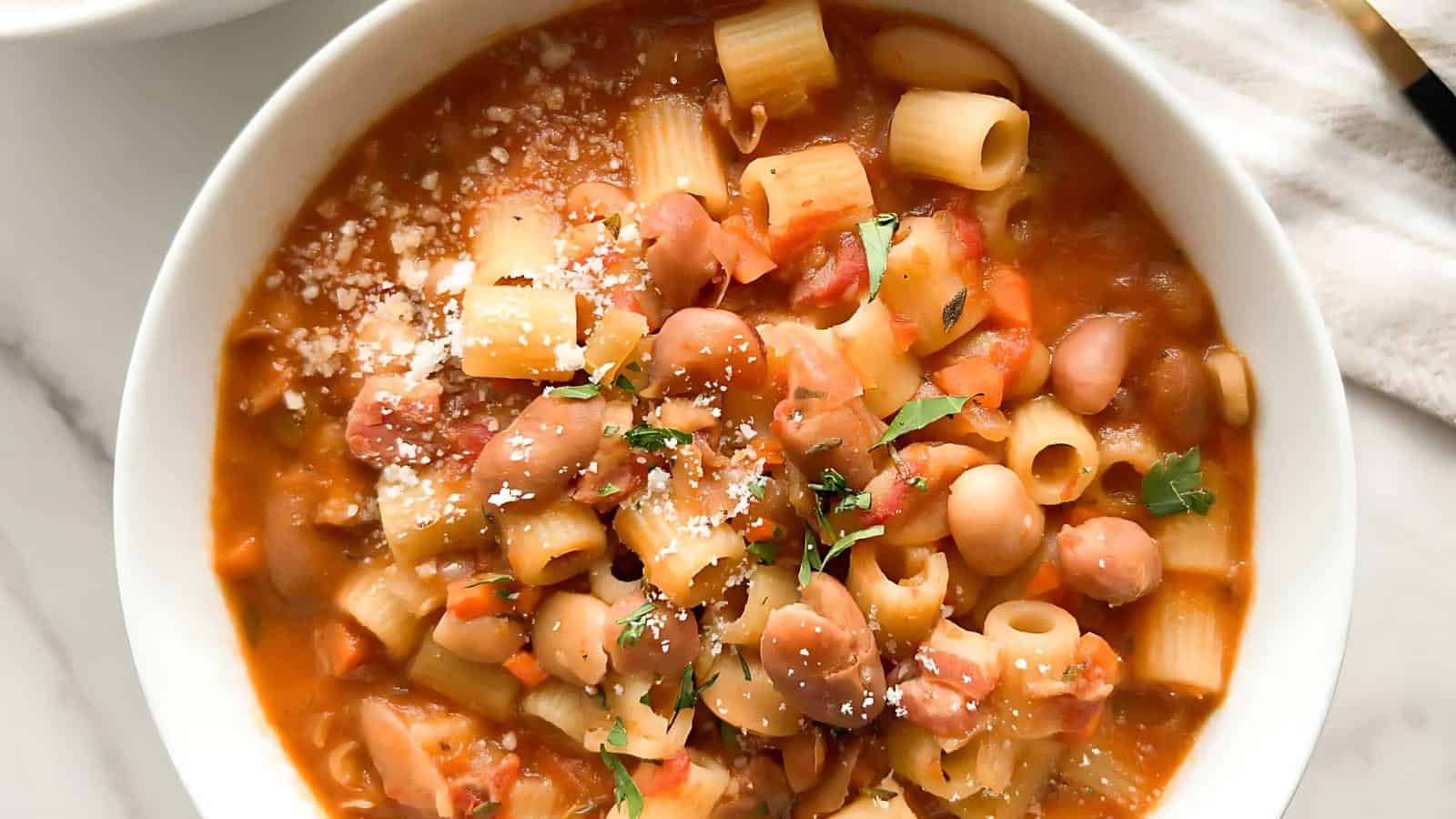 A bowl of pasta with beans in a tomato-based sauce, garnished with grated cheese and parsley.