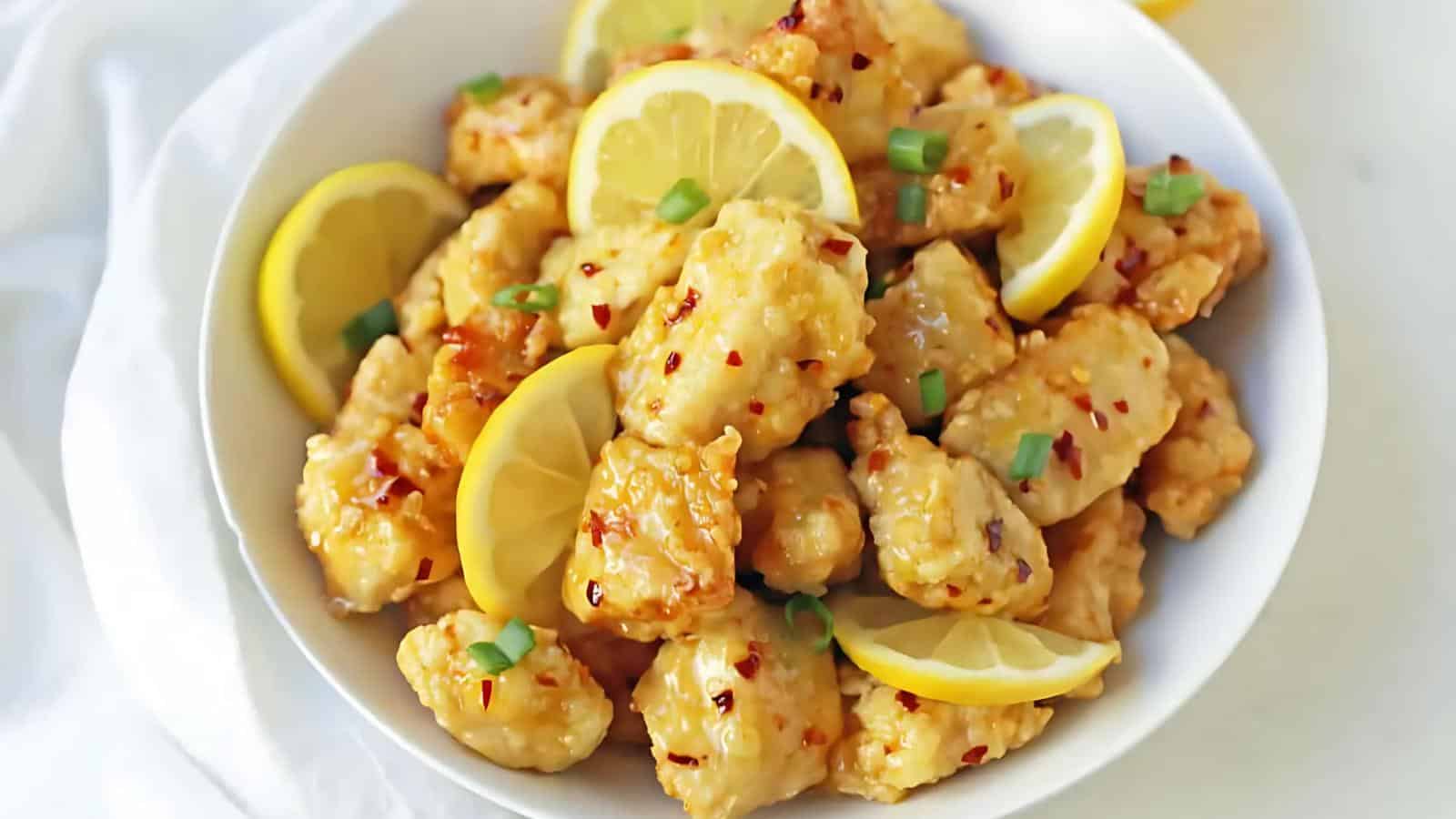 A bowl of fried shrimp garnished with sliced lemon, chopped green onions, and red pepper flakes.