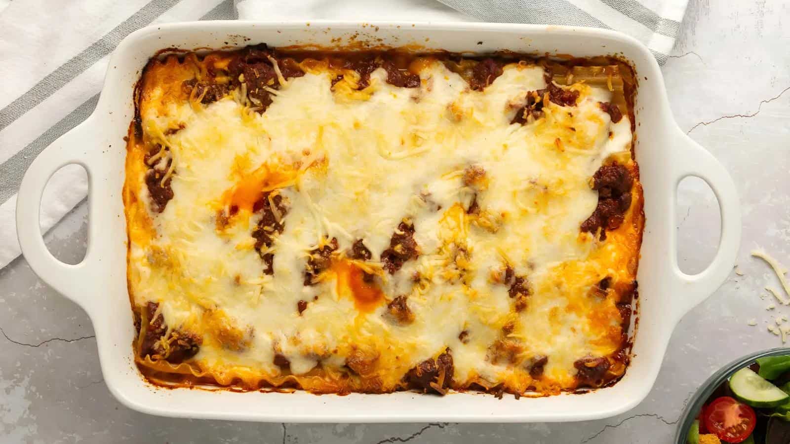 A baked dish of lasagna with melted cheese on top, in a white rectangular casserole dish on a marble surface.
