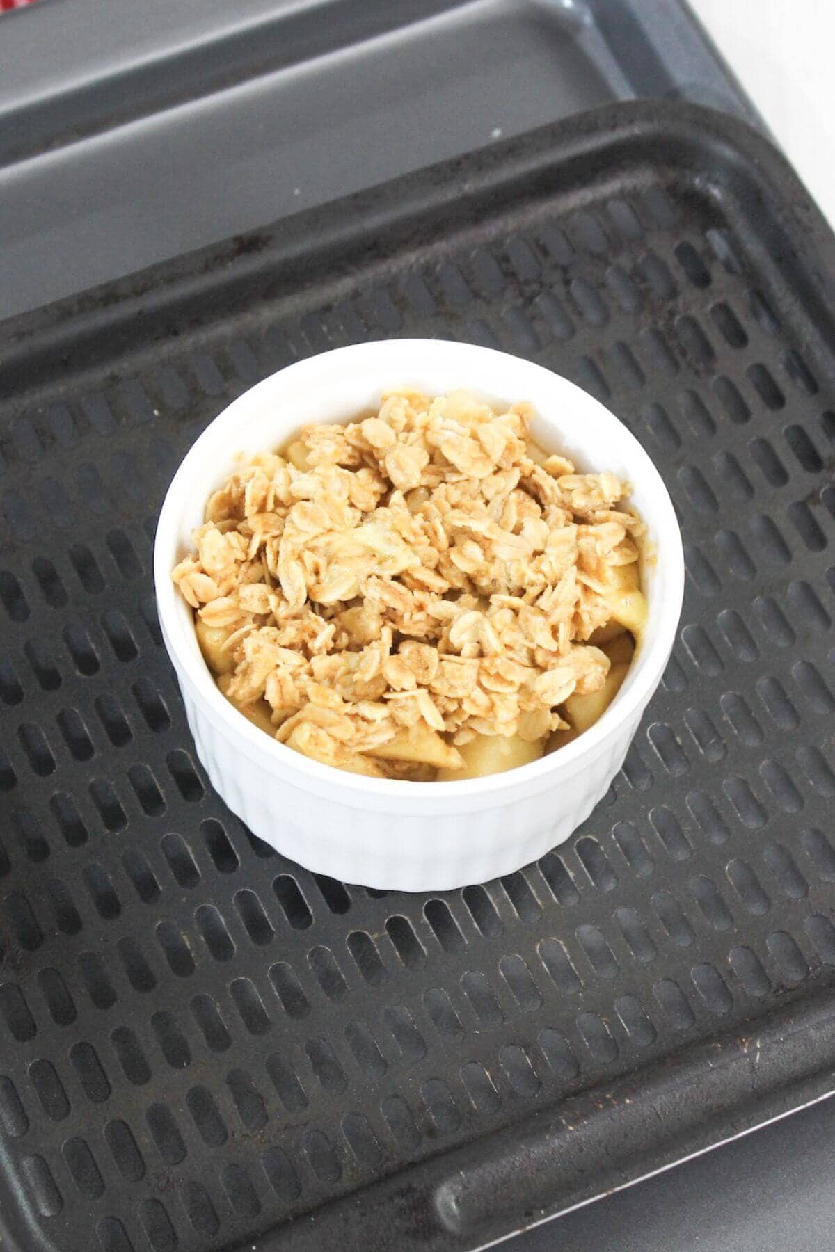 A white ramekin filled with a granola-topped dish is placed on a black baking tray.