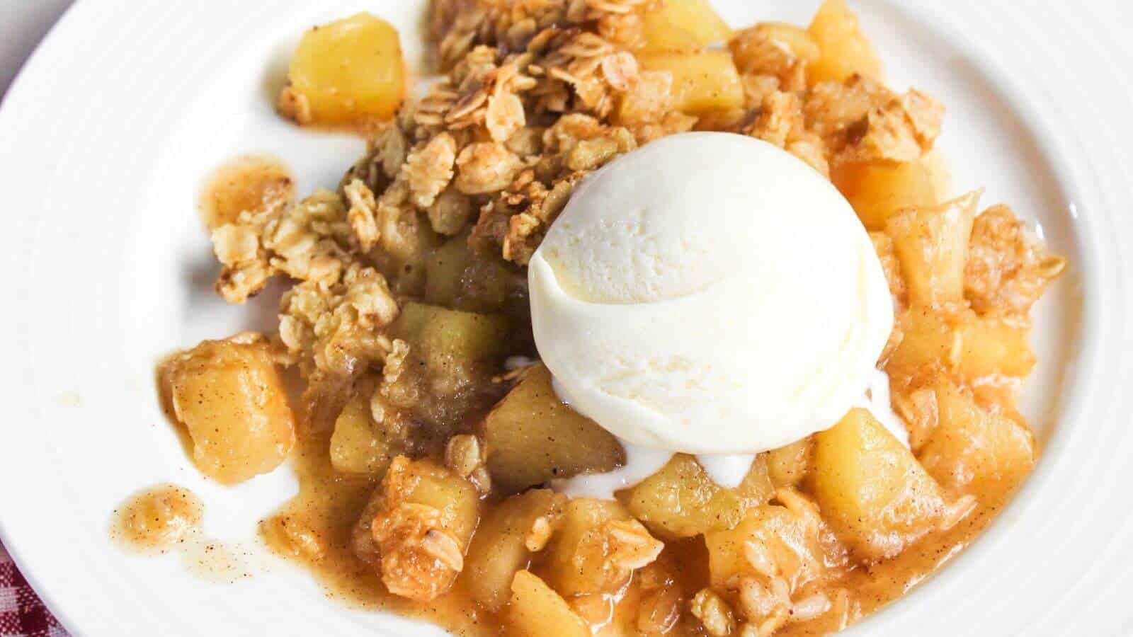 A plate of apple crumble topped with a scoop of vanilla ice cream. The crumble includes chunks of baked apples and a crumbly oat mixture.