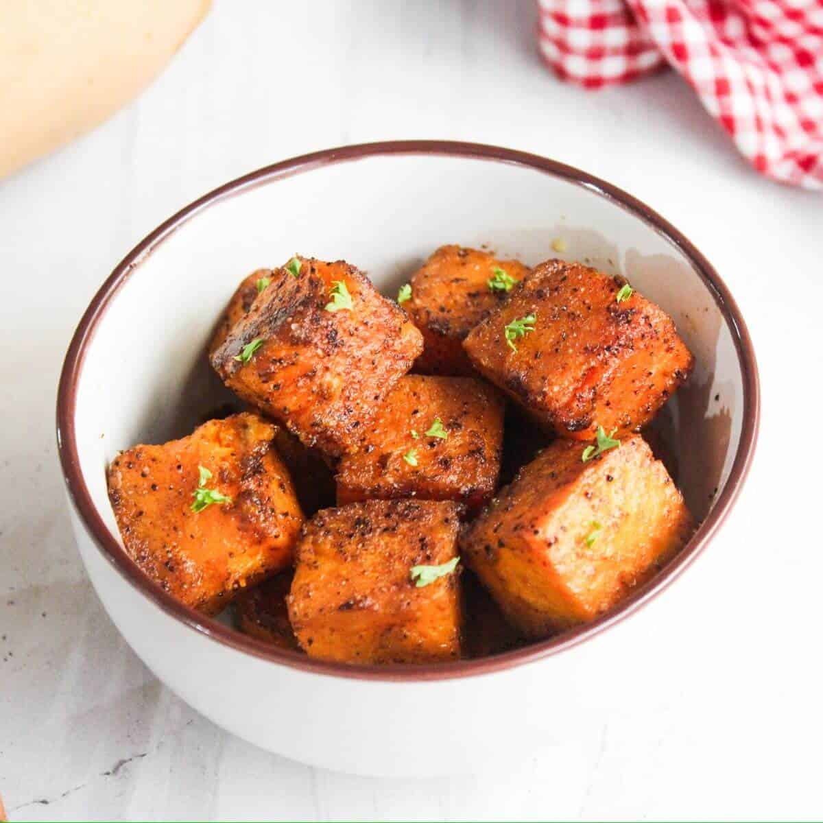 A bowl of seasoned and roasted sweet potato cubes garnished with herbs.