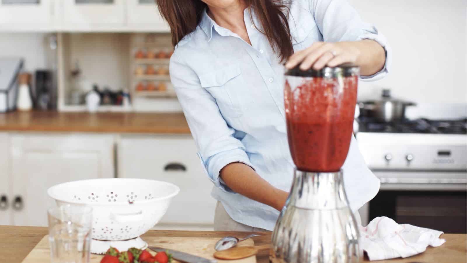 Person using a blender to make a strawberry smoothie in a kitchen.