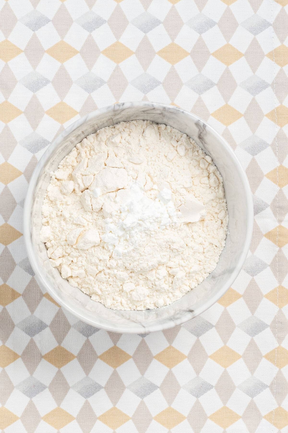 A bowl filled with flour, placed on a patterned surface.