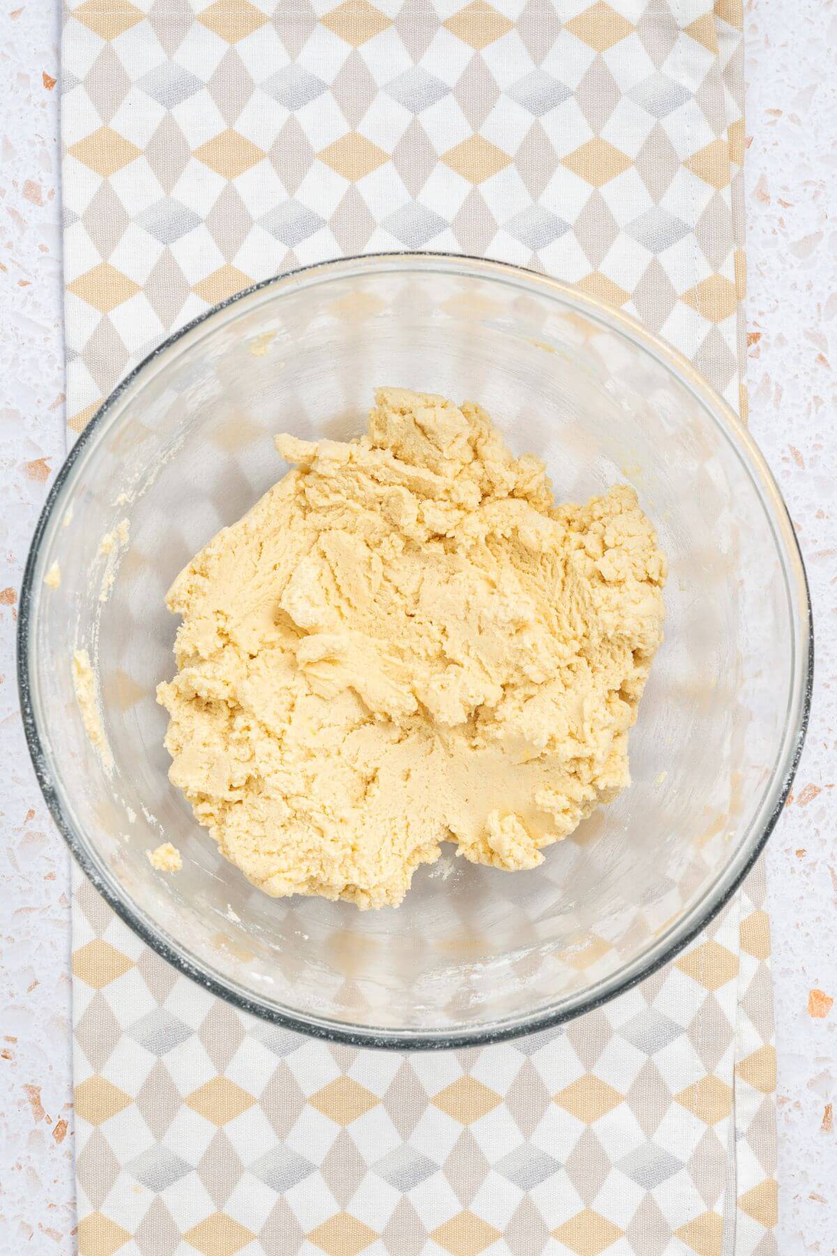 A glass bowl containing a dough mixture on a patterned cloth.