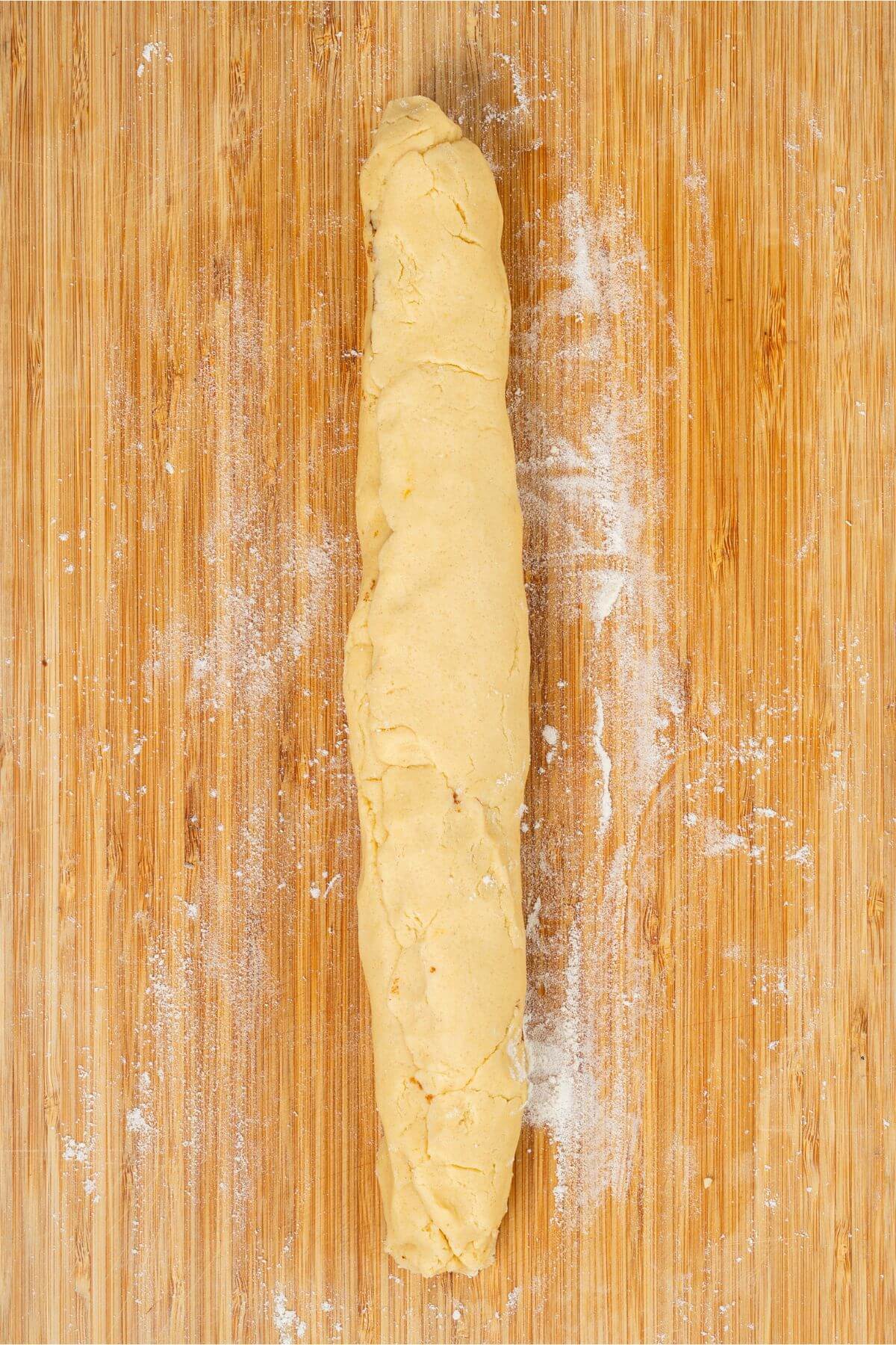 A roll of cookie dough on a floured wooden surface.