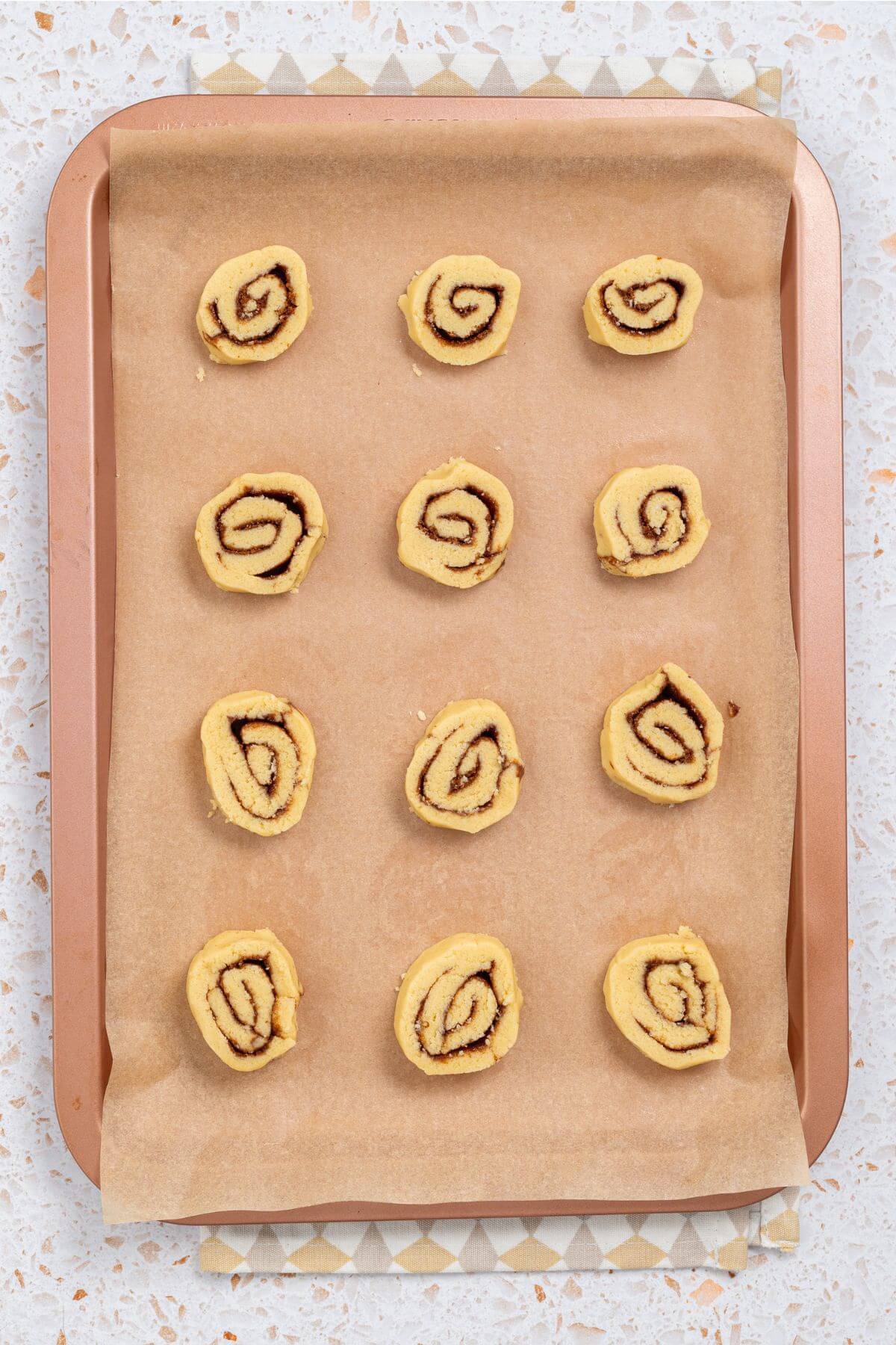 Unbaked cinnamon roll dough pieces arranged on a parchment-lined baking sheet.