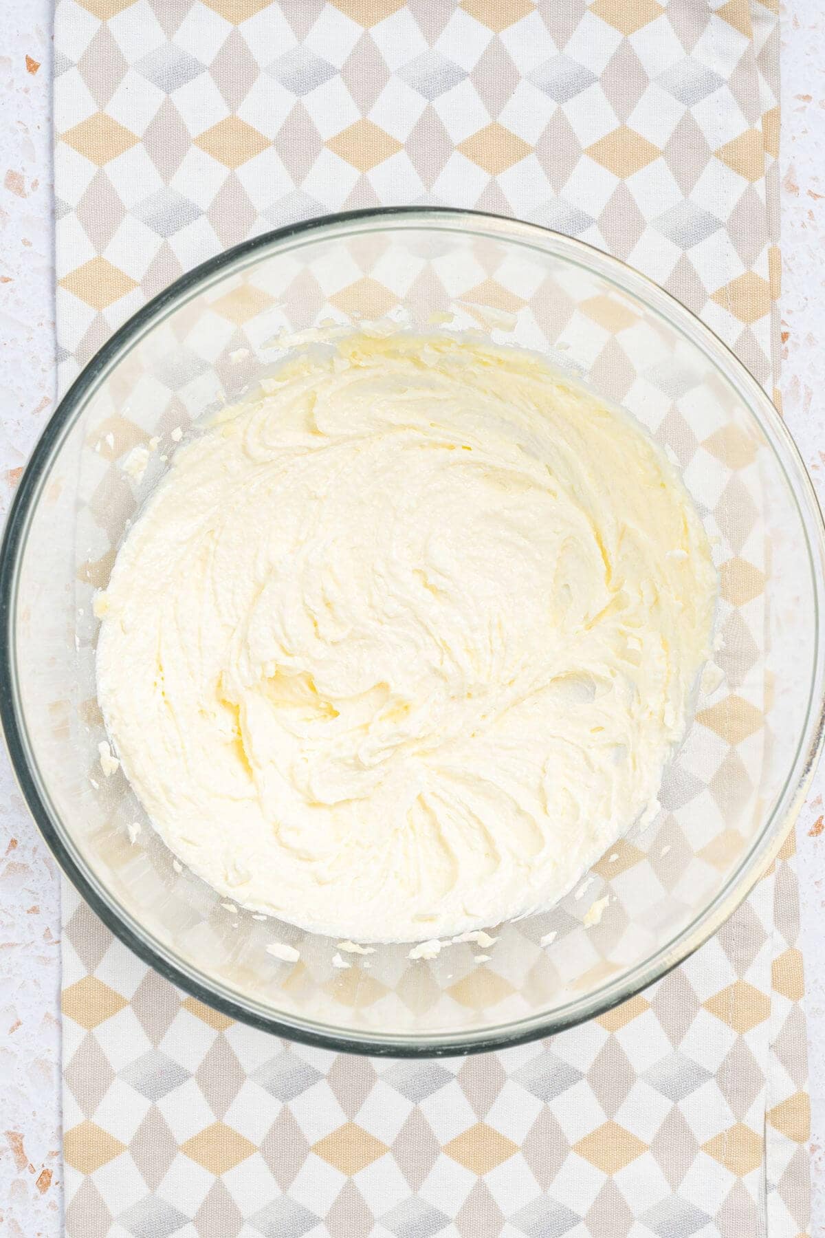 A clear glass bowl filled with whipped cream resting on a patterned cloth.