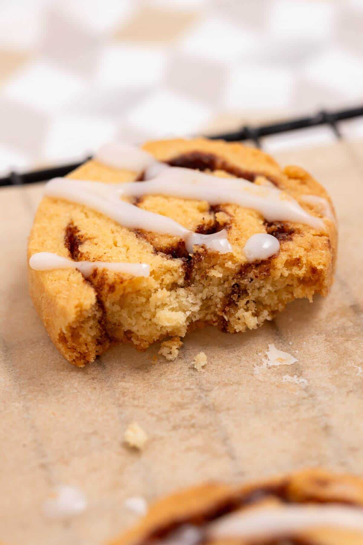 A partially eaten cinnamon cookie with white icing drizzle on parchment paper.
