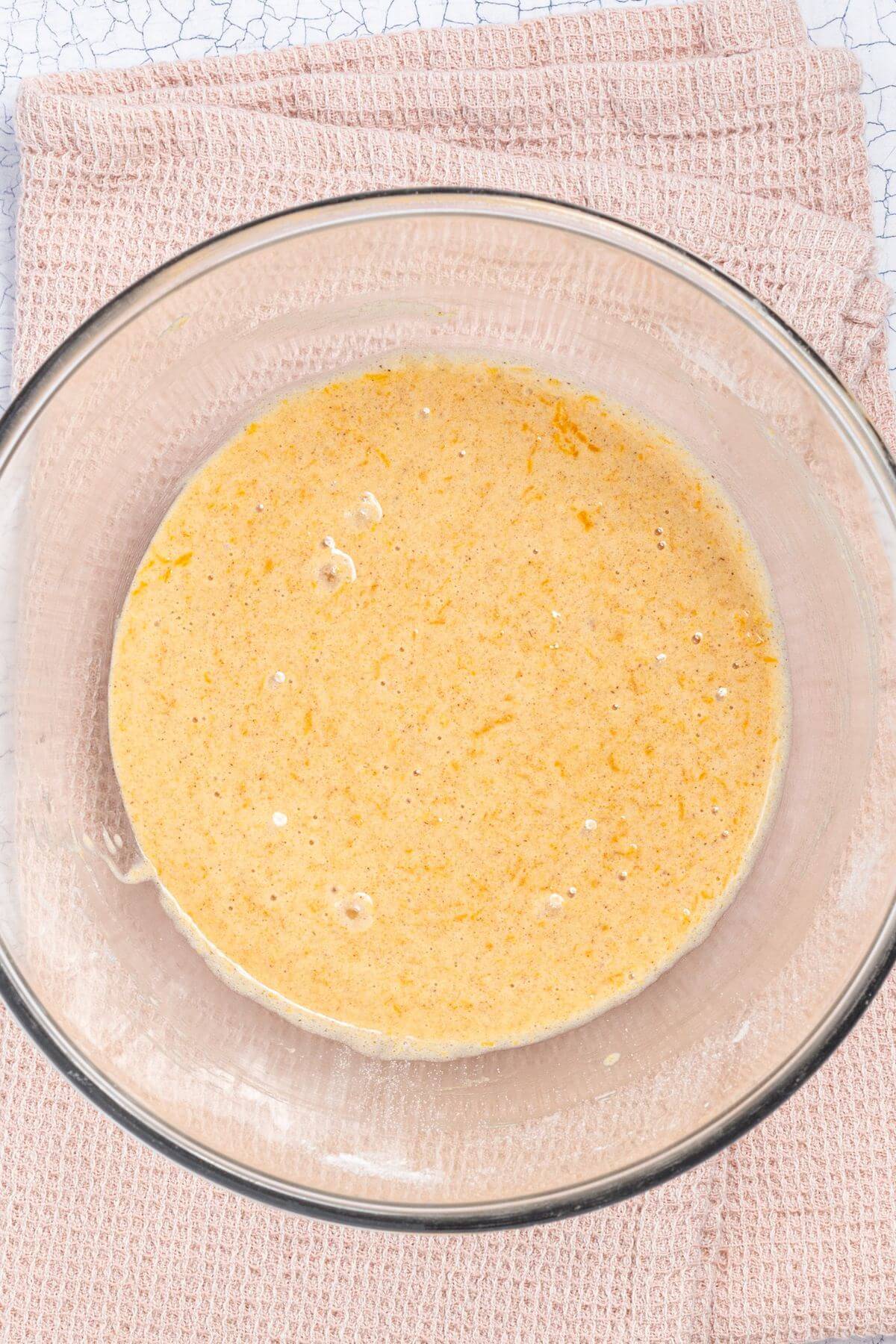 A glass bowl containing a mixture of ingredients is placed on a textured, light pink cloth.