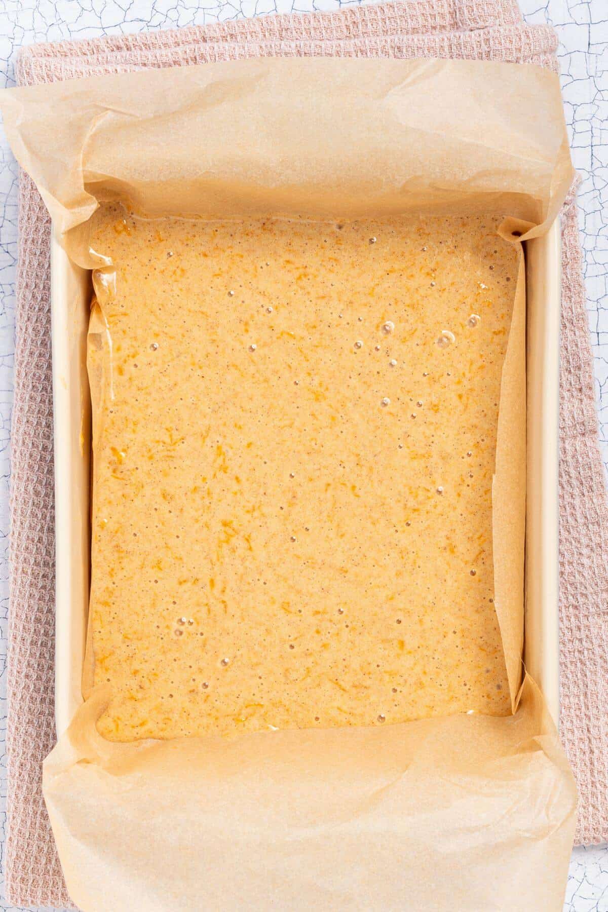 A baking dish lined with parchment paper and filled with uncooked batter, ready to be baked.
