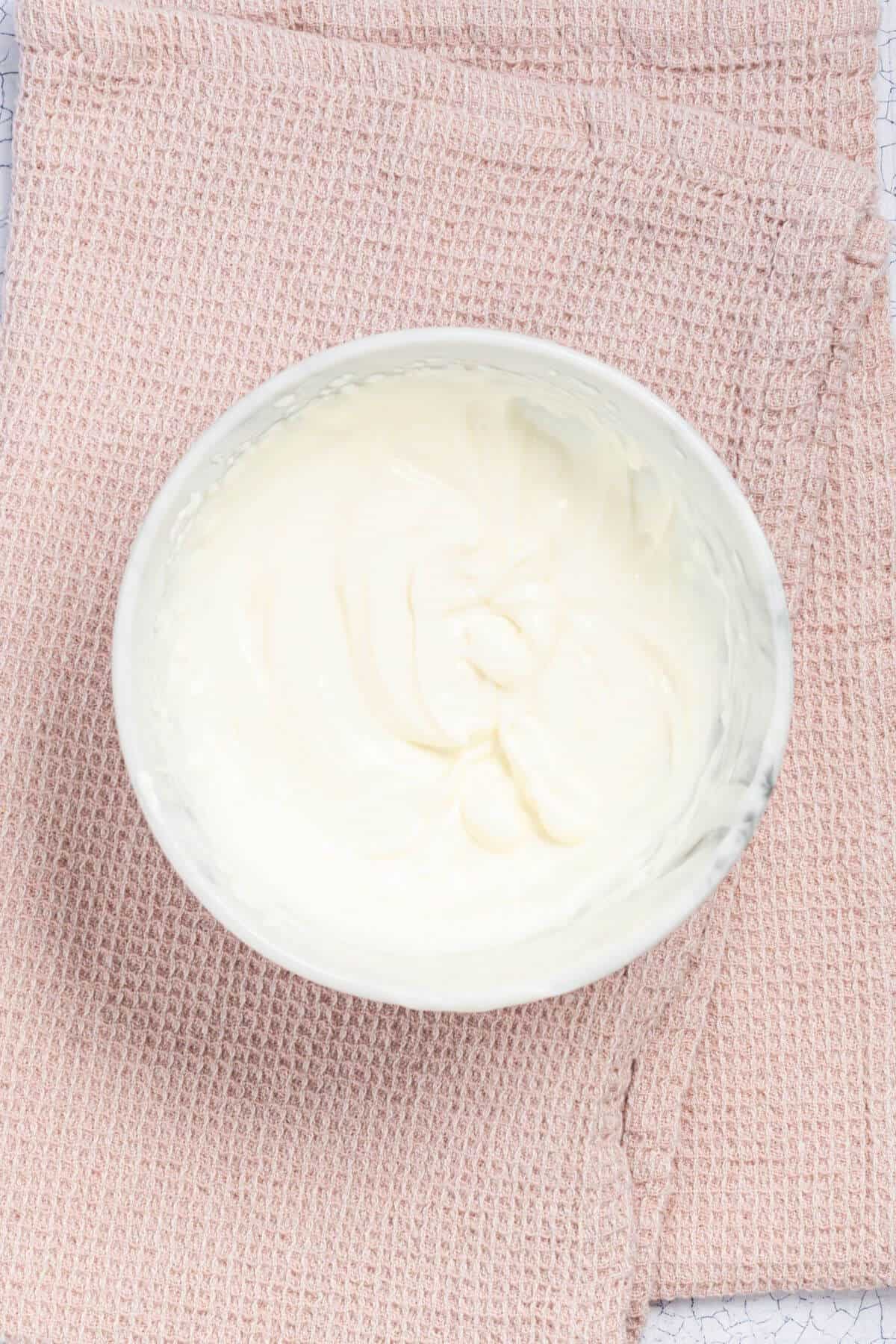 A bowl filled with creamy white yogurt placed on a folded pink textured cloth.