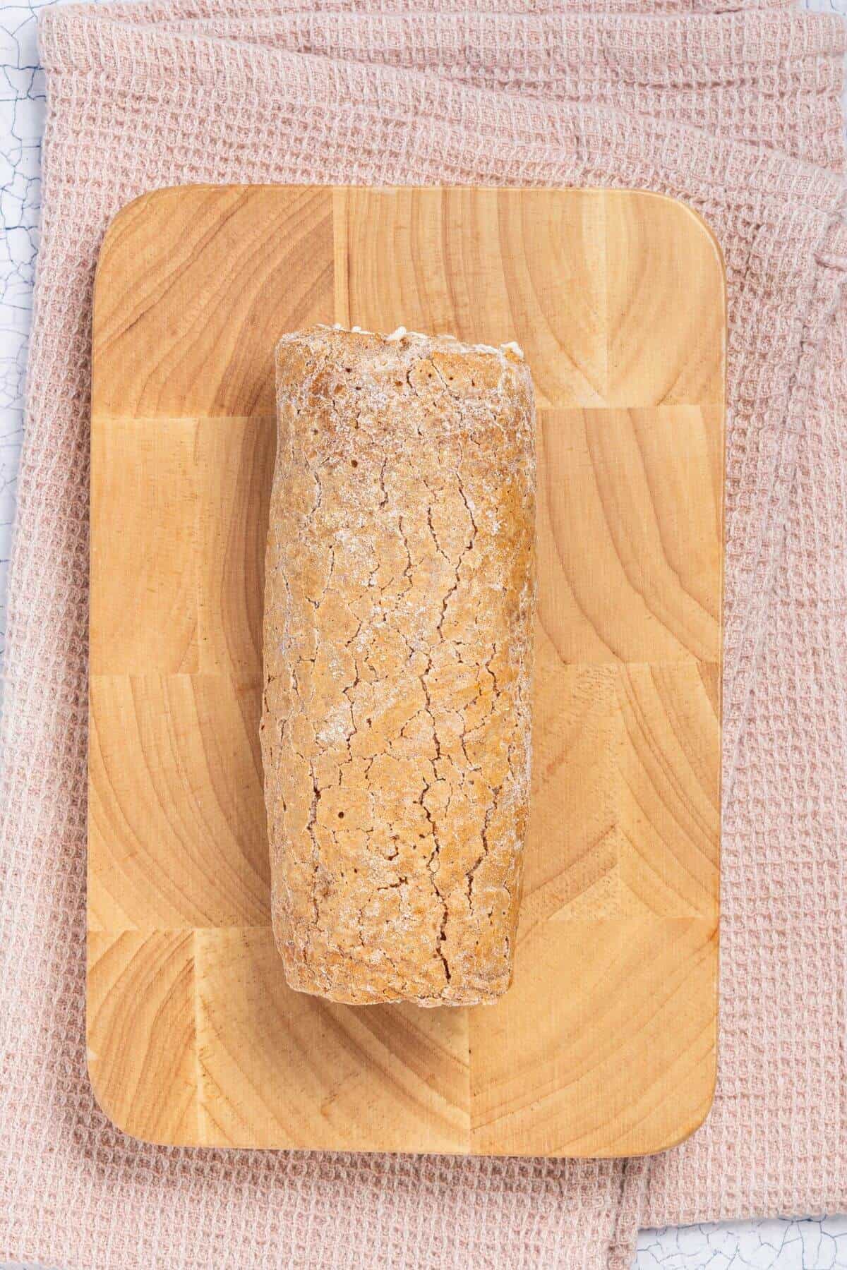 A single loaf of crusty bread sits on a wooden cutting board placed on a textured cloth.