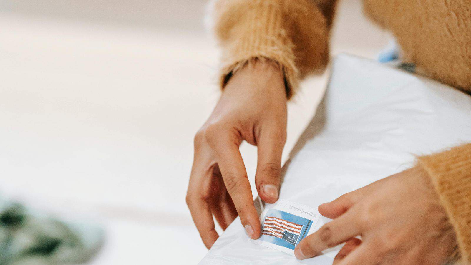 A person affixes an American flag stamp onto a white envelope.