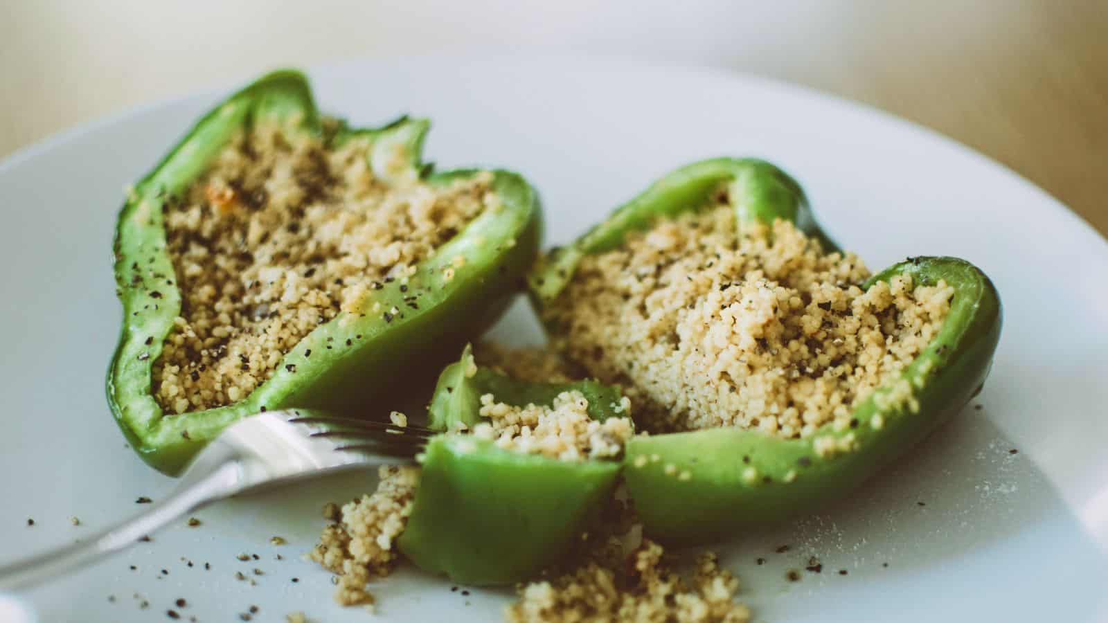 Green bell pepper halves filled with couscous and seasoning on a white plate, with a fork nearby.