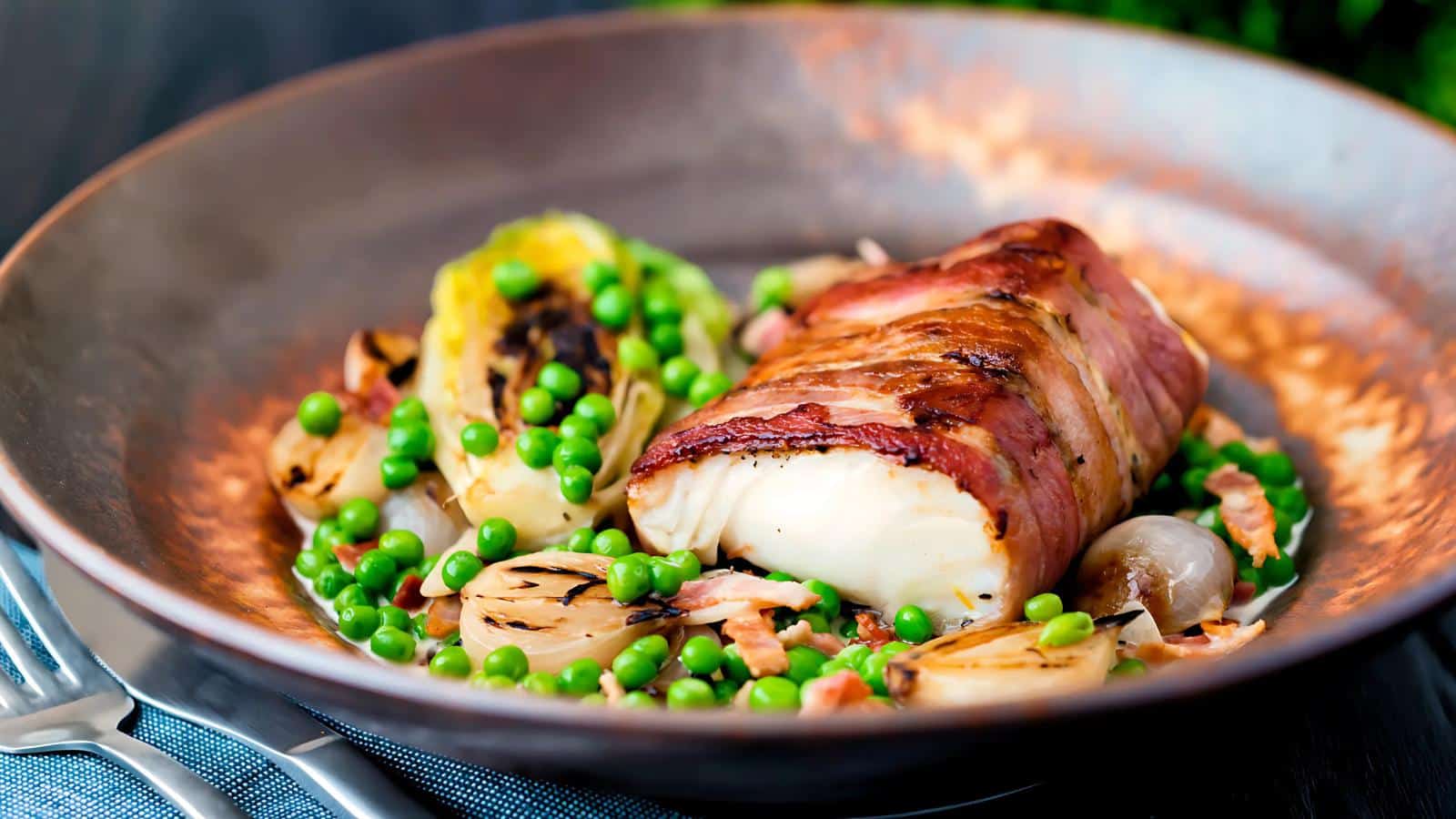 A dish featuring bacon-wrapped fish served on a plate with peas, grilled vegetables, and onions.
