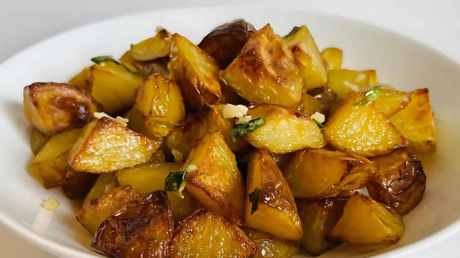 A white bowl filled with roasted potato wedges garnished with herbs and small garlic pieces.